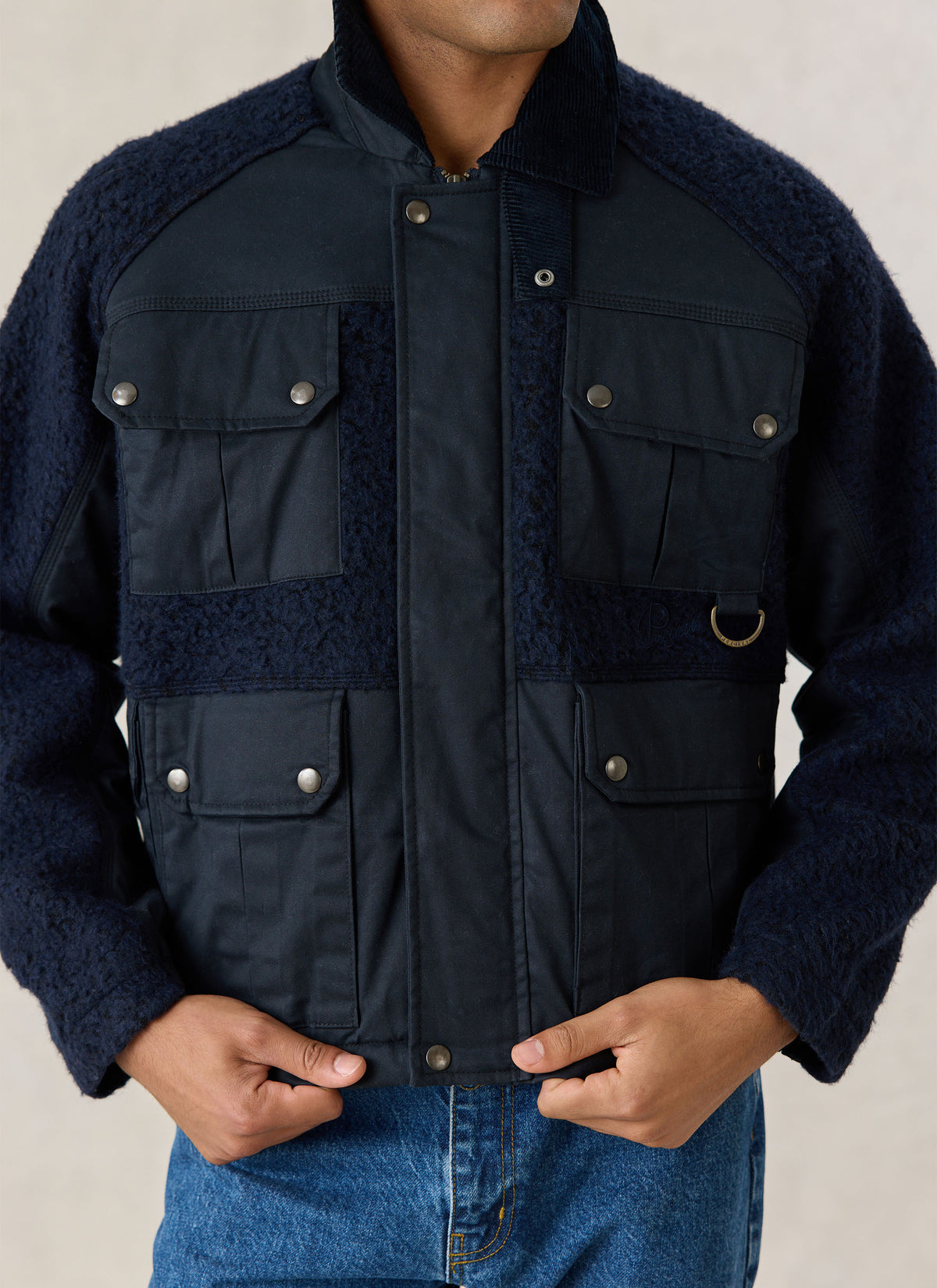 A close-up of the Percival navy Fletcher utility jacket showing four flap pockets and contrasting textured panels.