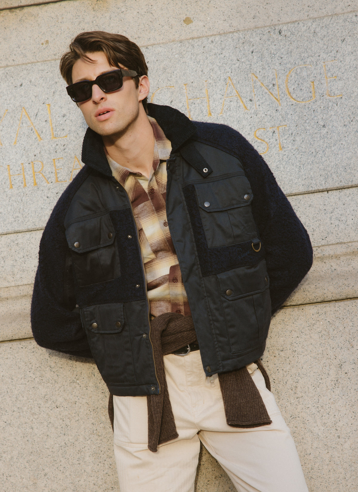 A model wearing the Percival brown checked western shirt layered under a dark jacket and sunglasses outdoors.