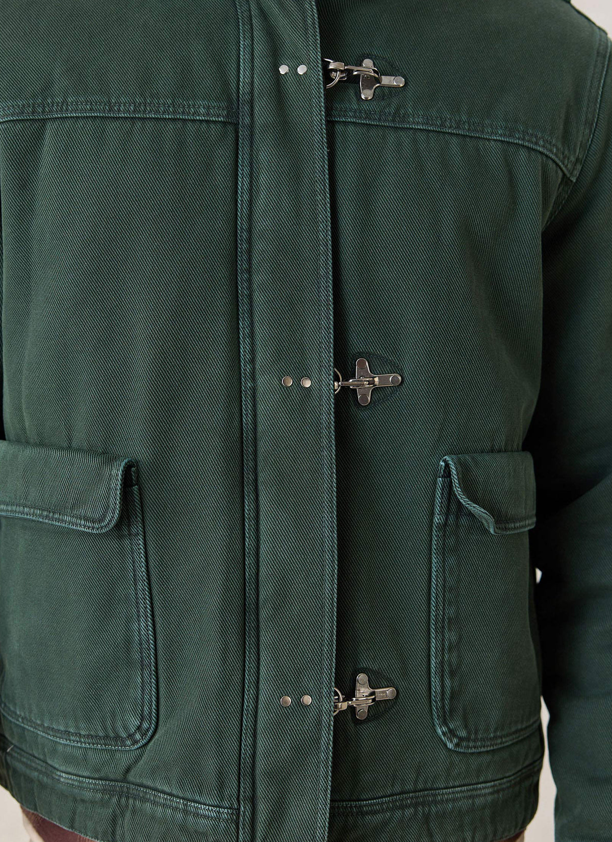 A close-up of the forest green Percival Fontane cotton jacket highlighting the metal fireman clasps and front pockets.