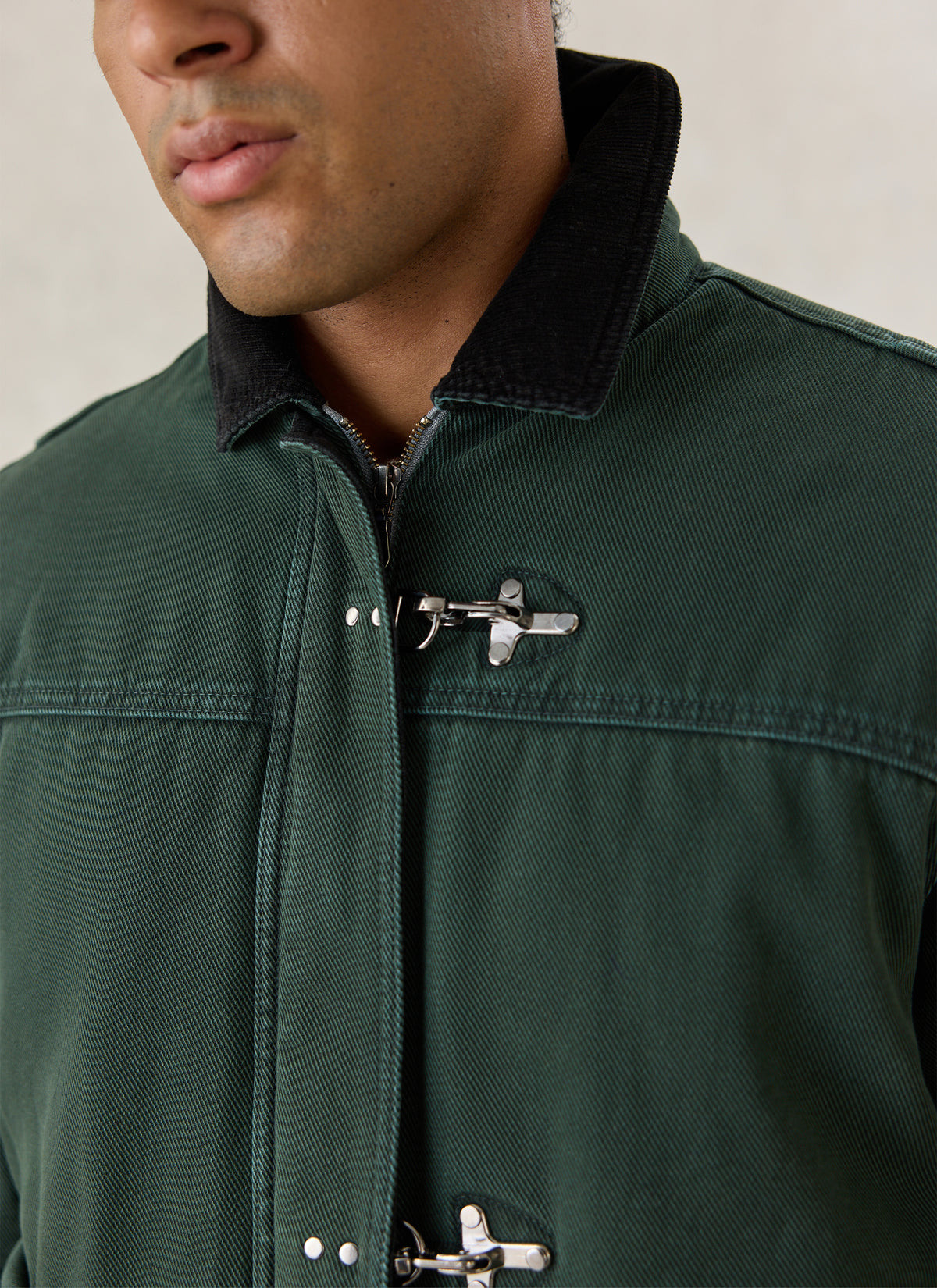 Close-up of forest green Percival Fontane cotton jacket, showing the metal fireman clasp, zip front, and contrast collar.
