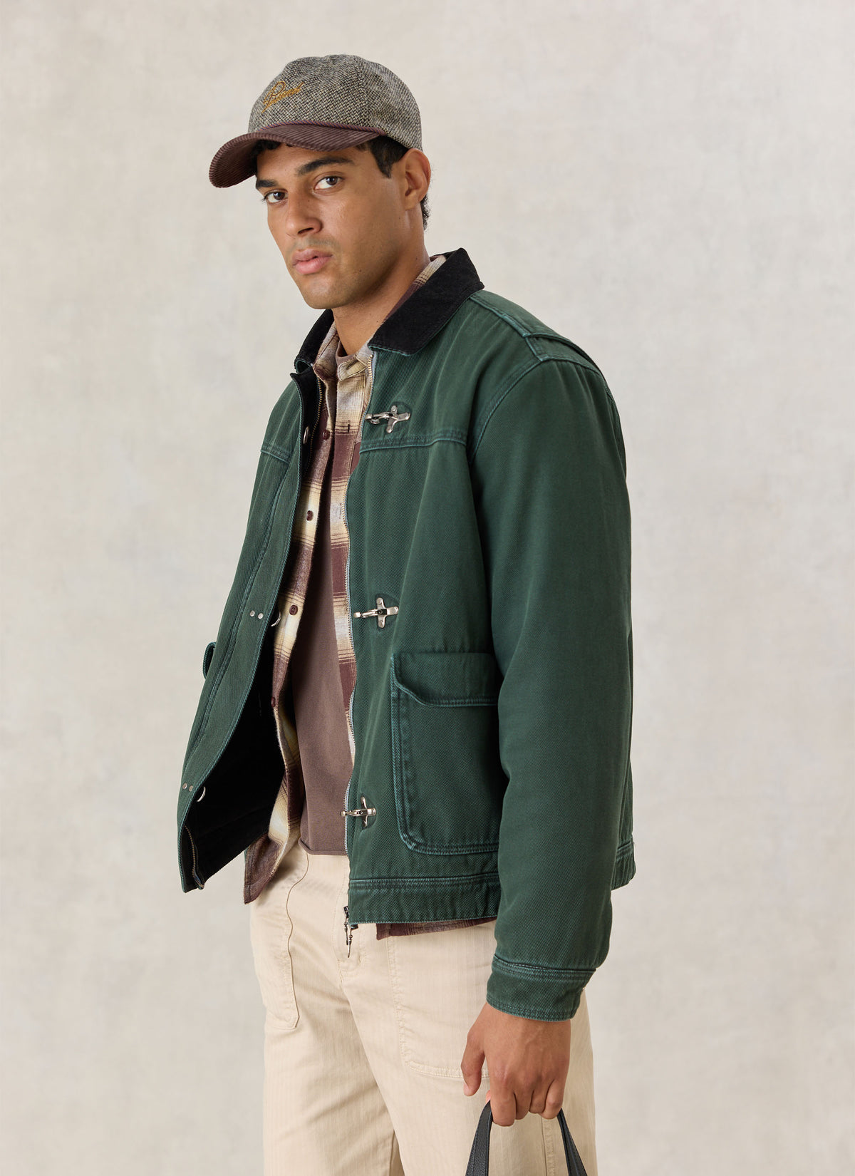 A model wearing the forest green Percival Fontane cotton fireman clasp jacket over a patterned shirt and light trousers.