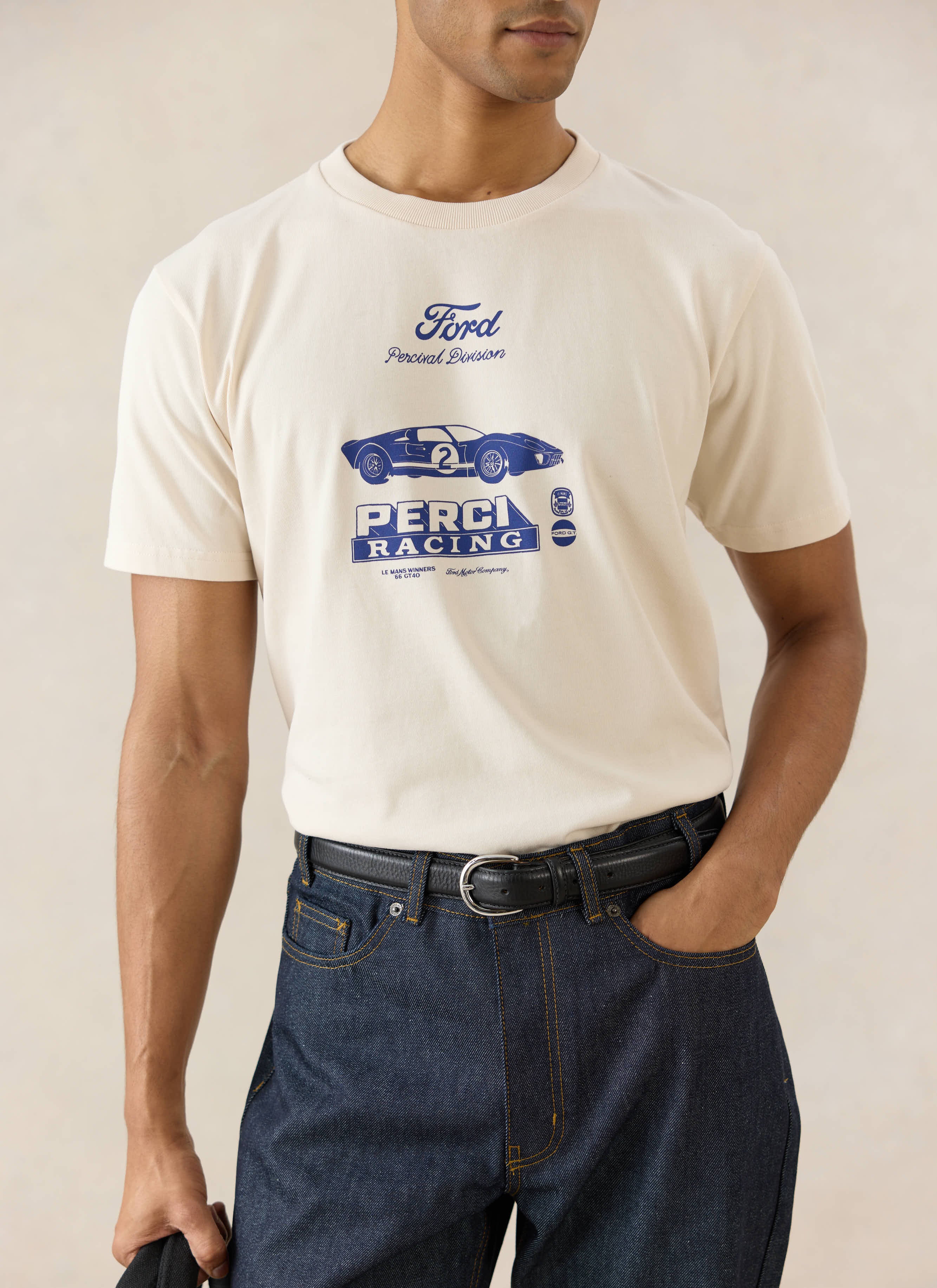 Percival cream Ford GT40 Archive T-shirt with a blue graphic, tucked into heritage raw denim jeans with a leather belt.