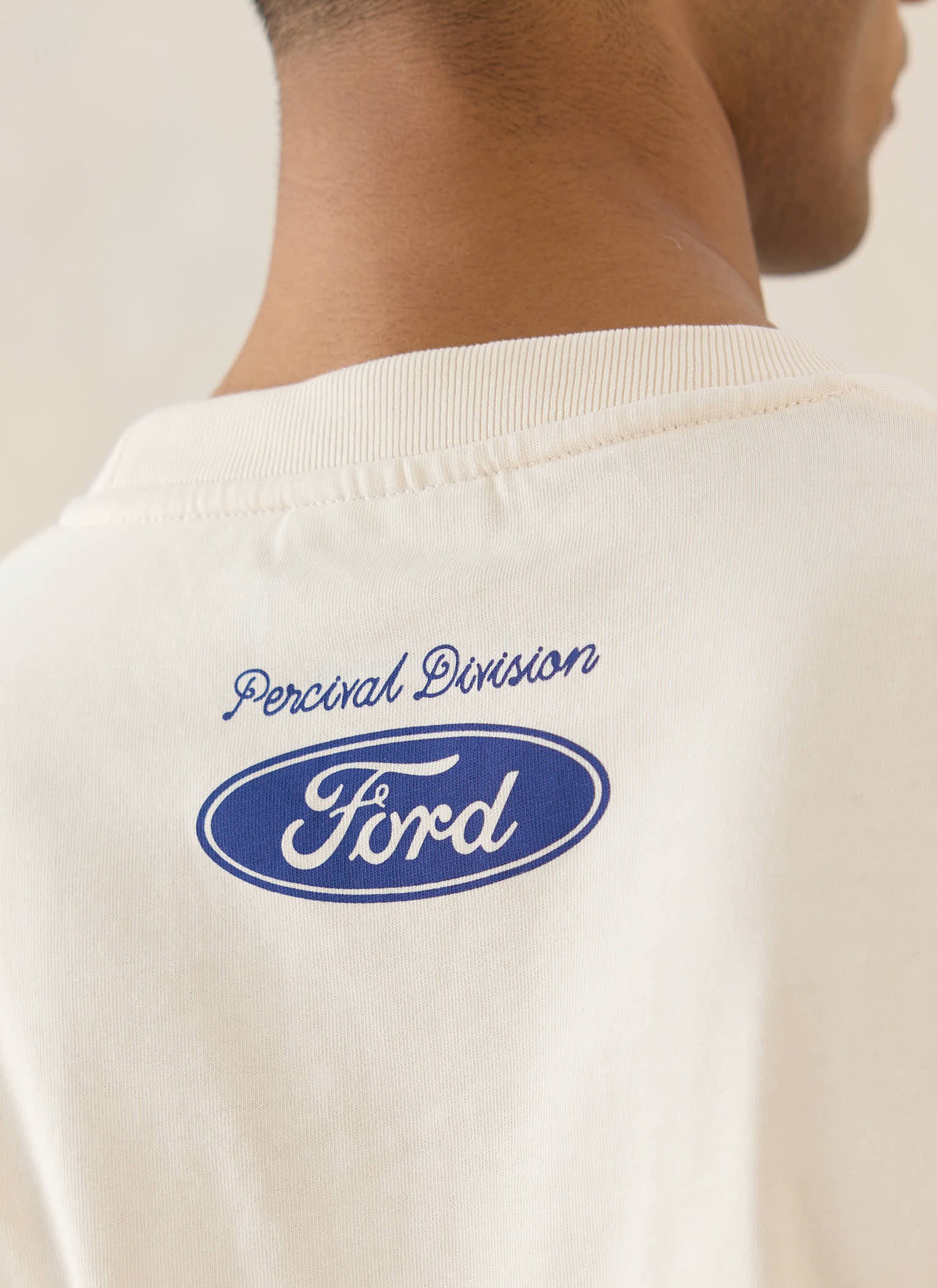 Close-up of the cream Percival x Ford GT40 t-shirt back neck, highlighting the blue collaborative logo and script.