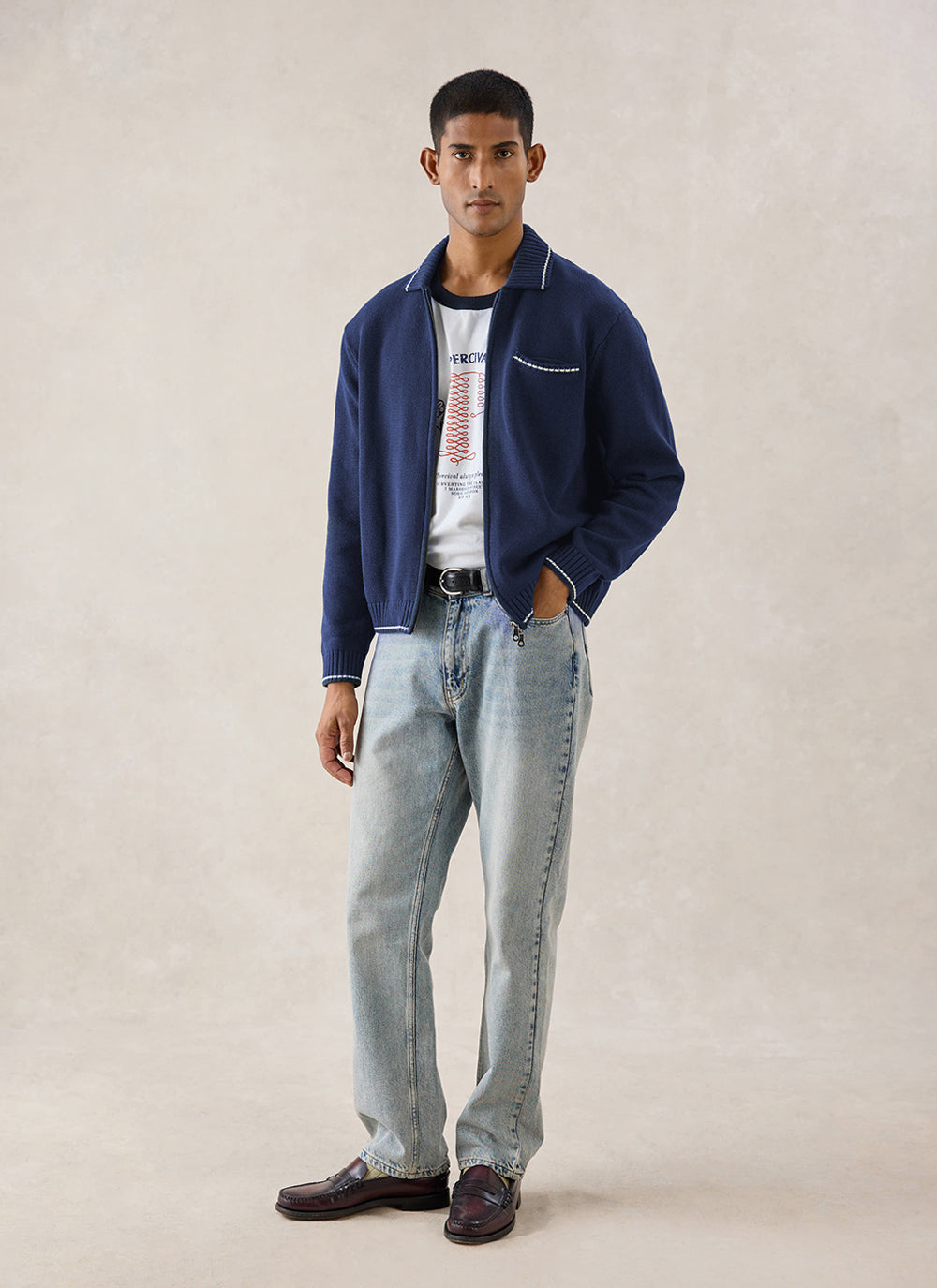 A model wears the navy Percival Gardner dense knitted zip cardigan in cotton over light-wash jeans with loafers.
