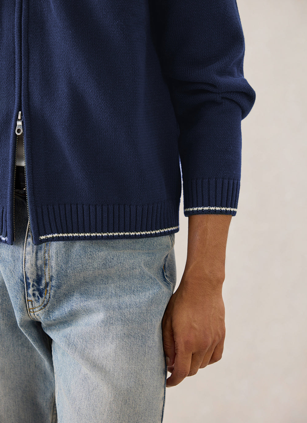 Close-up of a model wearing the Percival navy cotton zip-up cardigan with contrast stitching and light blue jeans.