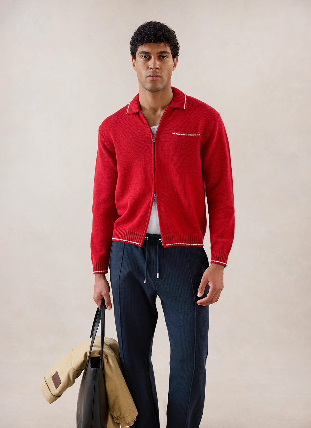Model wearing the red Percival Gardner dense knitted zip cardigan, holding a black bag and a jacket.