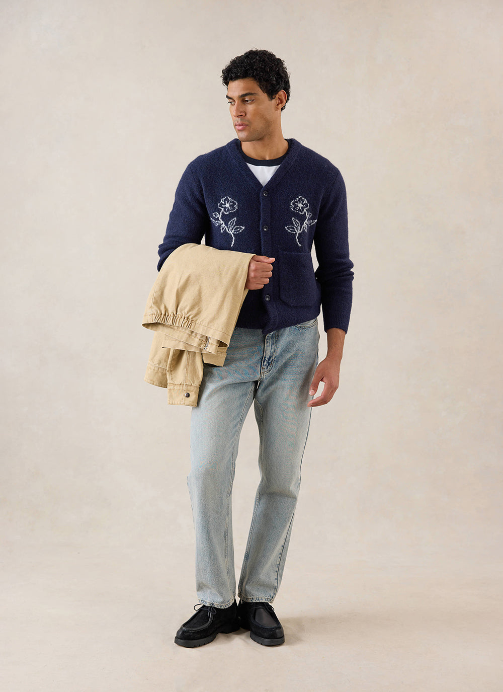 A model wears the navy Percival Gibson Boxy Jacquard Cardigan, styled with light blue jeans and holding a tan jacket.