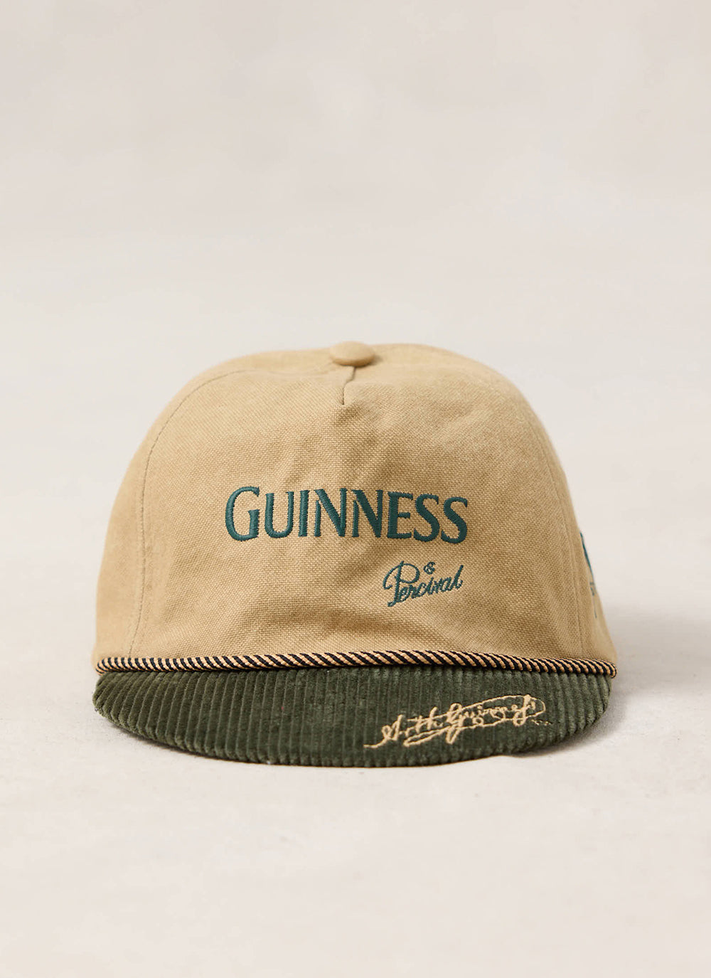 Front view of the beige Guinness x Percival short peak cap featuring green embroidery and a contrast green corduroy brim.