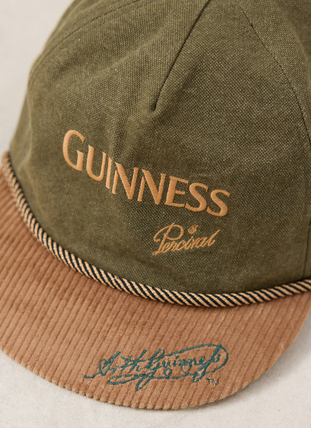 Close-up of the Guinness x Percival forest green cotton cap showing the embroidered branding and contrast cord peak.