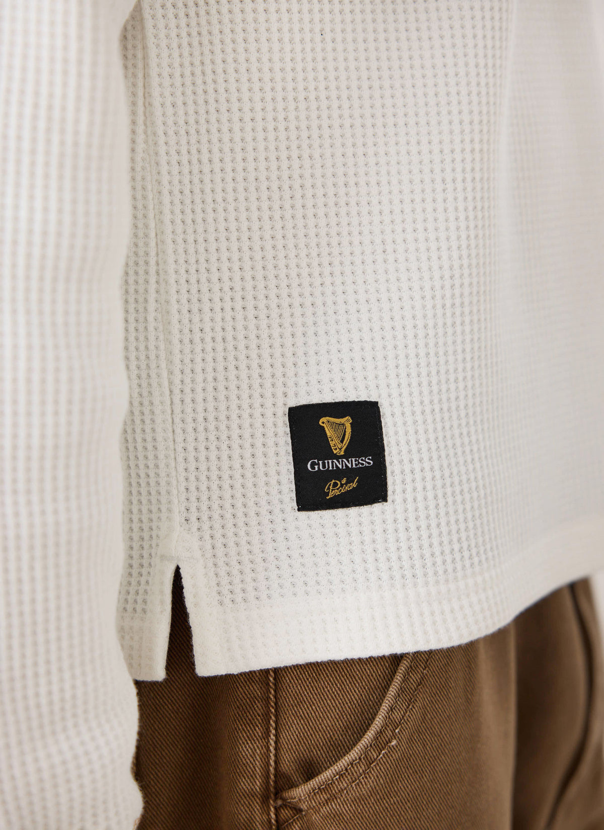 Close-up of the Guinness x Percival cream waffle henley showing the textured cotton fabric and lower woven brand label.
