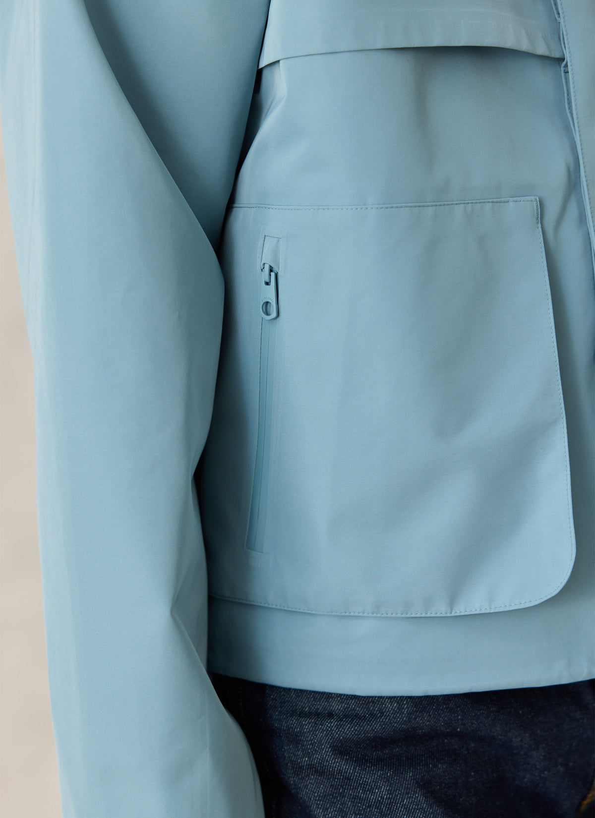 A close-up of the Percival Hanson waterproof rain jacket in light blue, showing the front pocket and zippered detail.