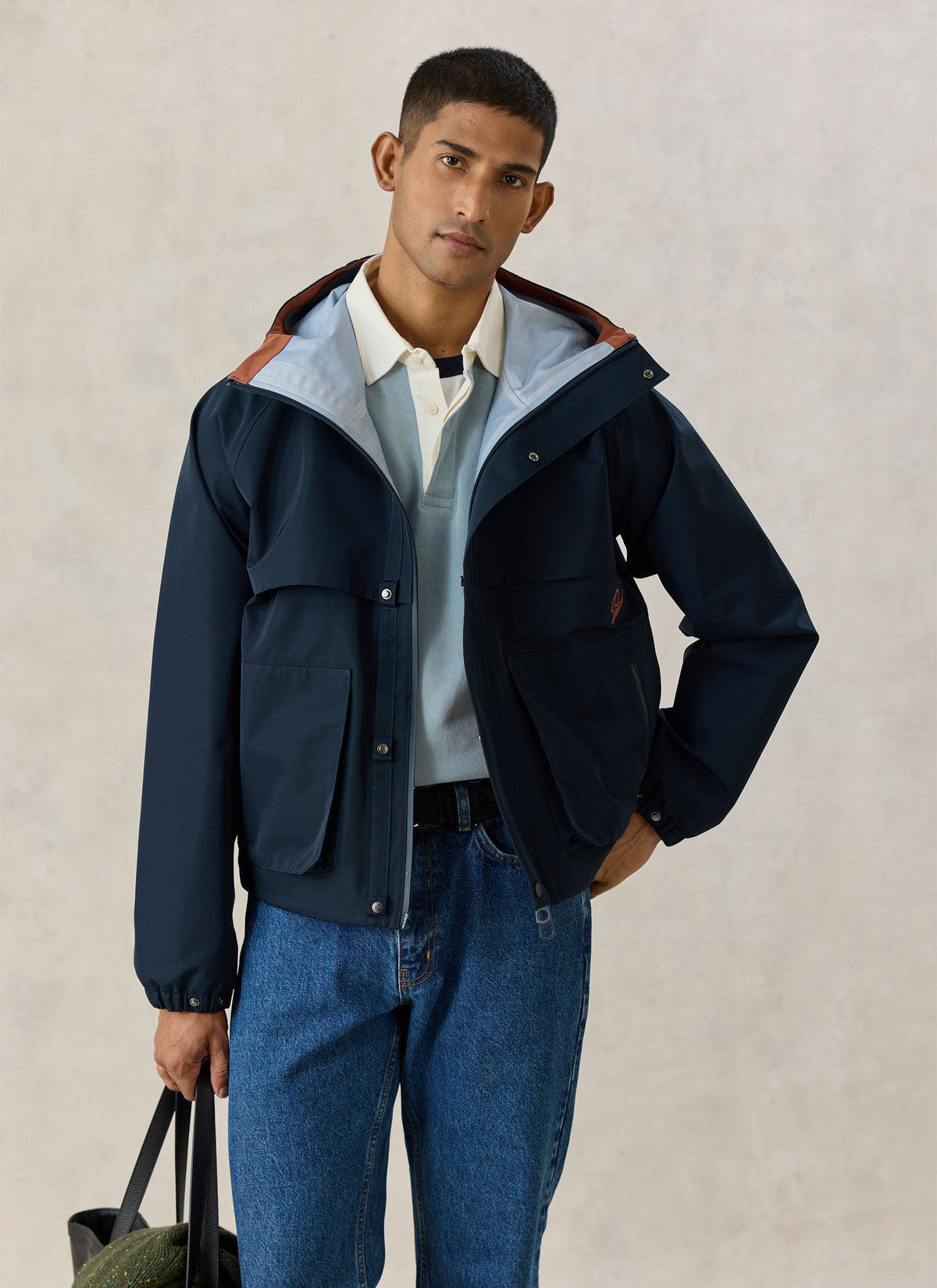 Model wearing the Percival navy blue Hanson boxy waterproof rain jacket with a hood and front pockets.