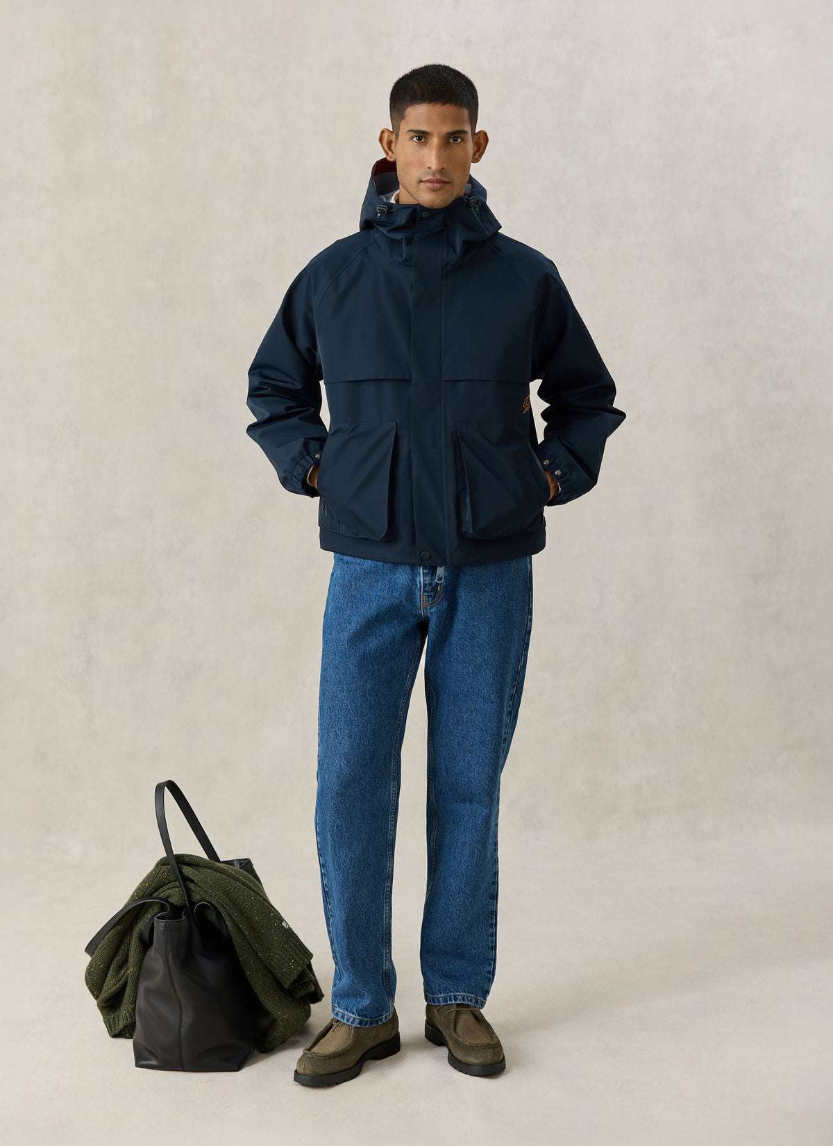 A model wearing the Percival navy blue Hanson waterproof rain jacket with a hood and large front pockets.