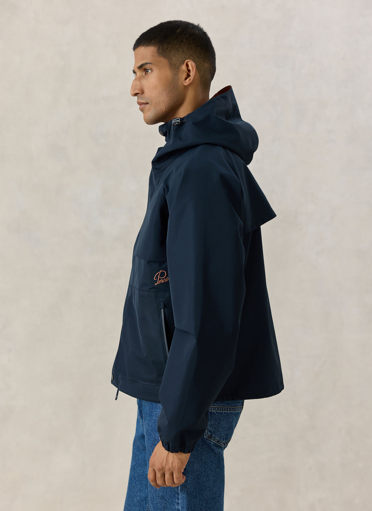 A model wearing the Percival navy blue Hanson waterproof rain jacket with a hood, viewed from the side.