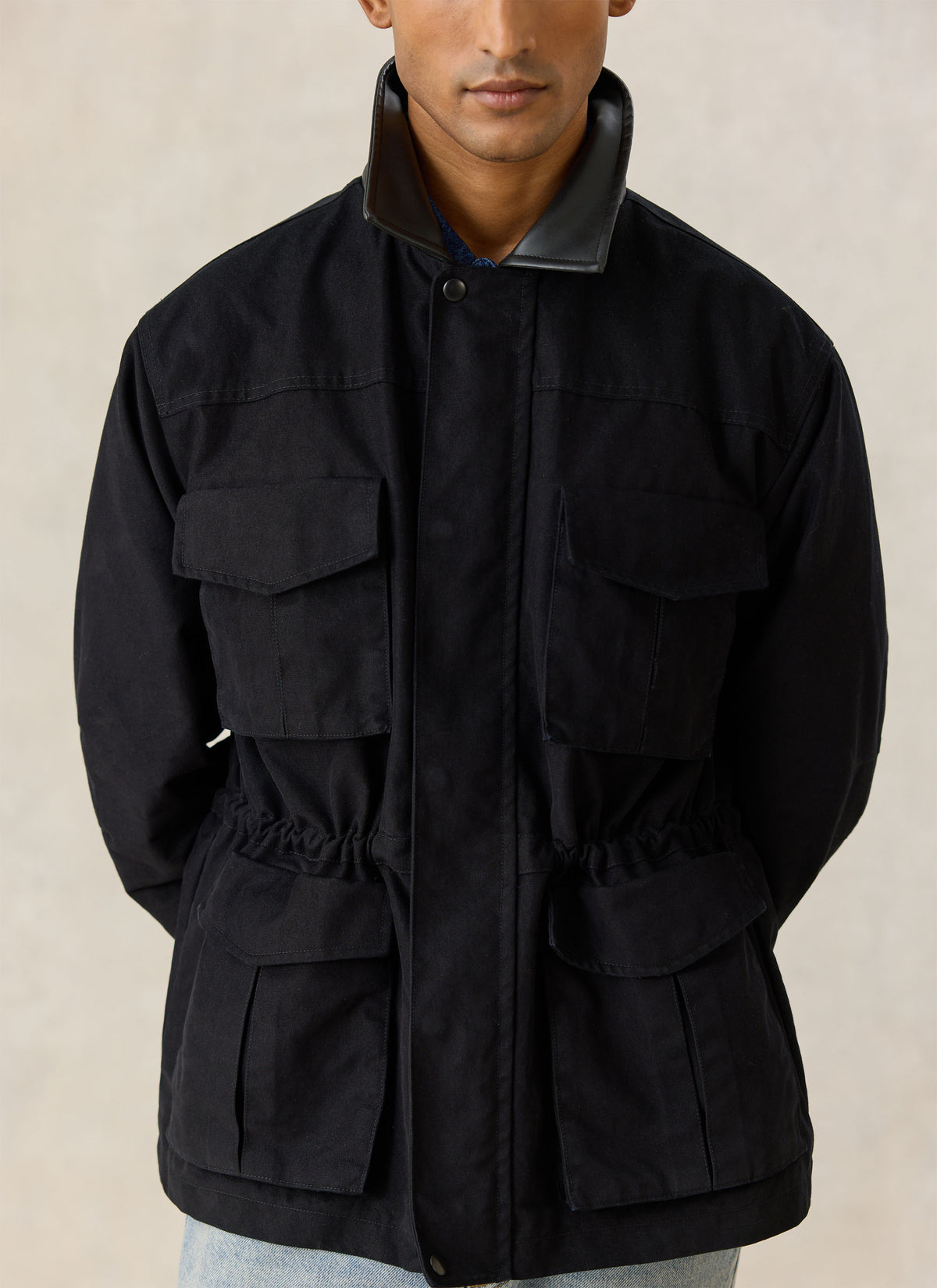 A model wearing the black Percival Harris Field Jacket, highlighting the front flap pockets and waist drawcord.