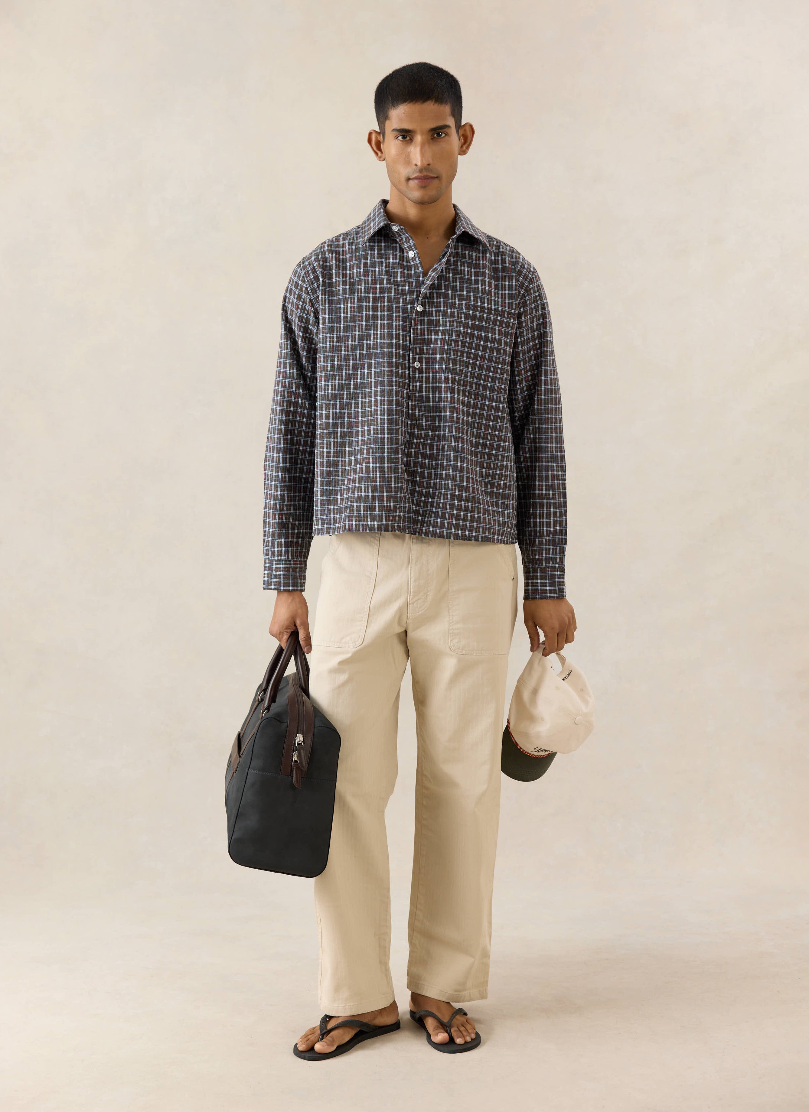 Percival Hinsley brown checked boxy shirt in cotton, worn by a model with beige trousers and a black bag.