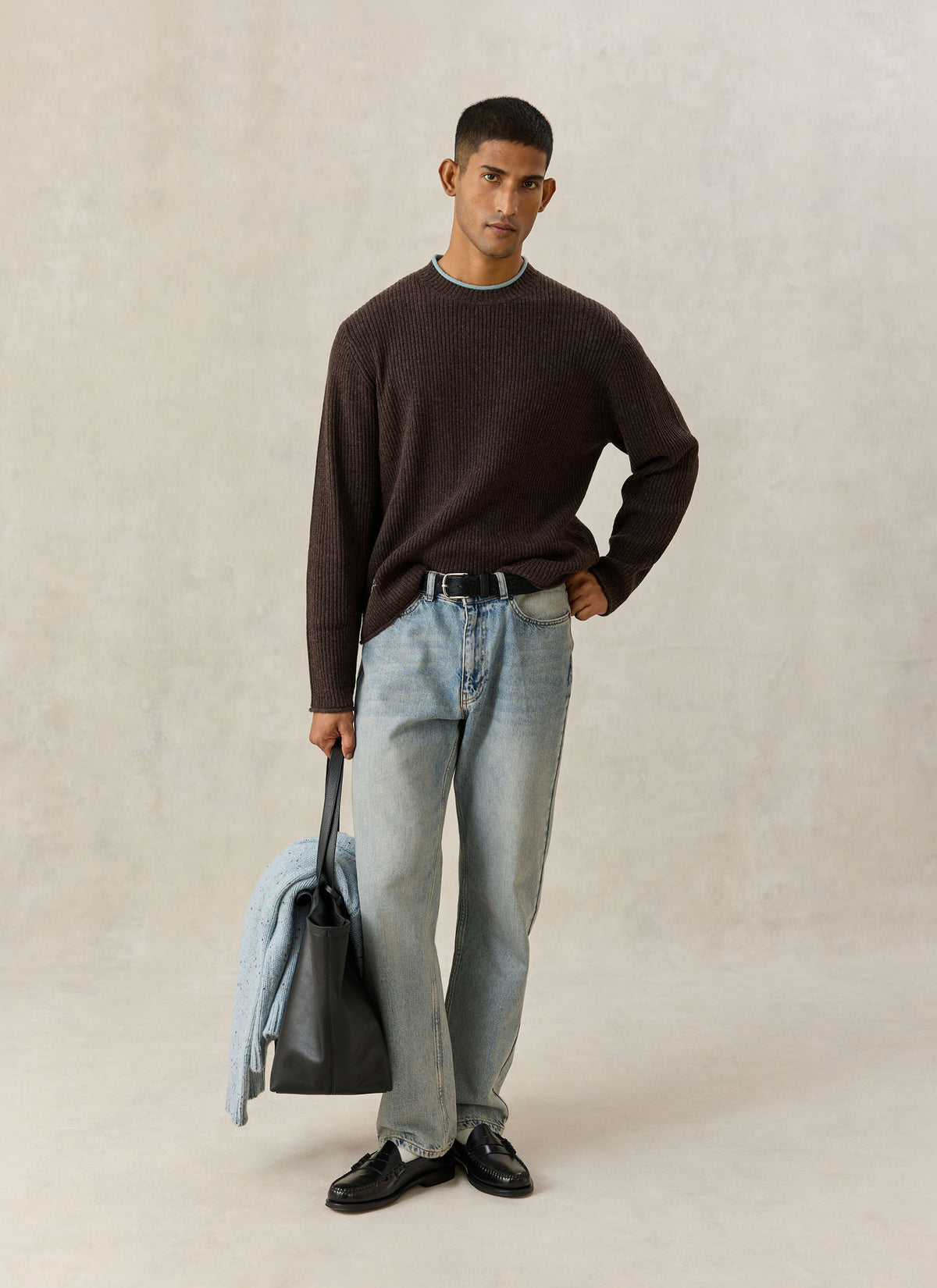 A model wearing the brown Percival Hurst ribbed knit wool-blend jumper with a light blue crew-neck trim and jeans.