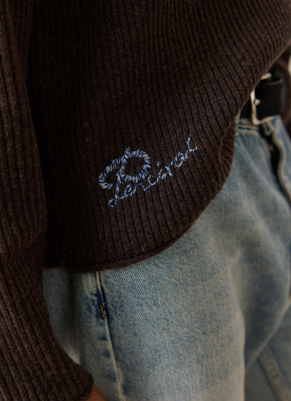 A close-up of the brown Hurst ribbed knit jumper showing the blue Percival embroidery at the hem.