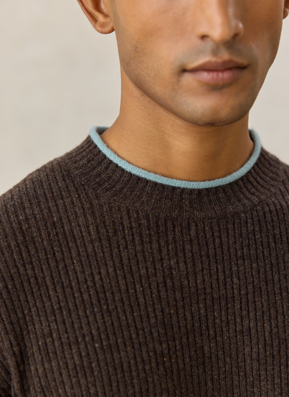 A close-up of a model wearing the Percival brown ribbed knit jumper, highlighting the contrasting blue crew-neck trim.