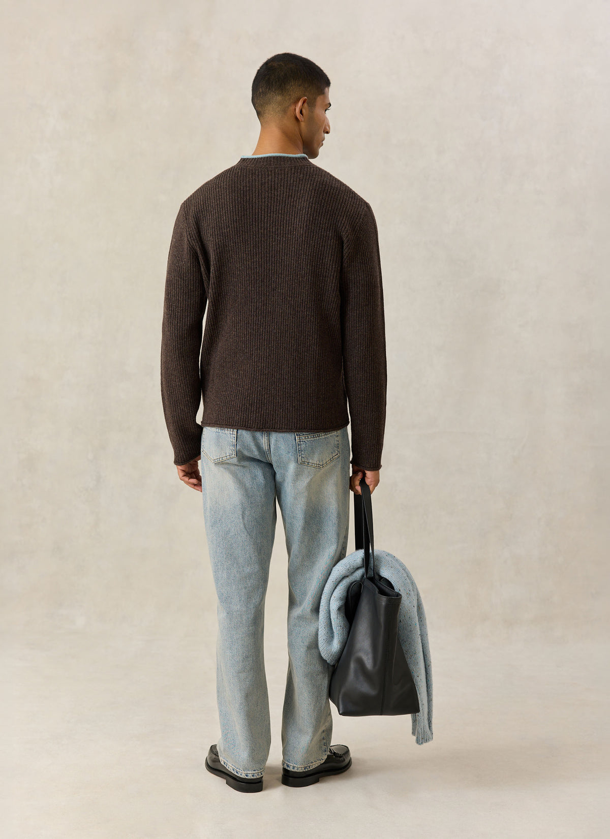 Model from behind wearing brown Percival Hurst knit jumper, jeans, and carrying a black bag.