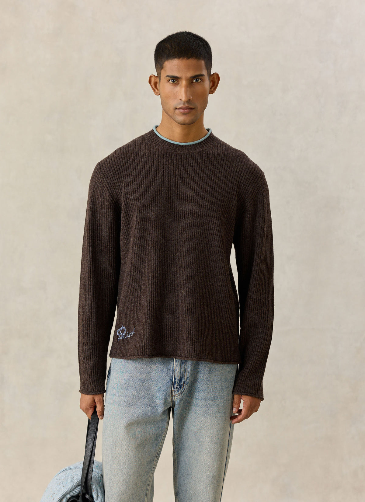 A model wearing the brown Percival Hurst ribbed knit wool-blend jumper with a blue crew-neck trim and jeans.