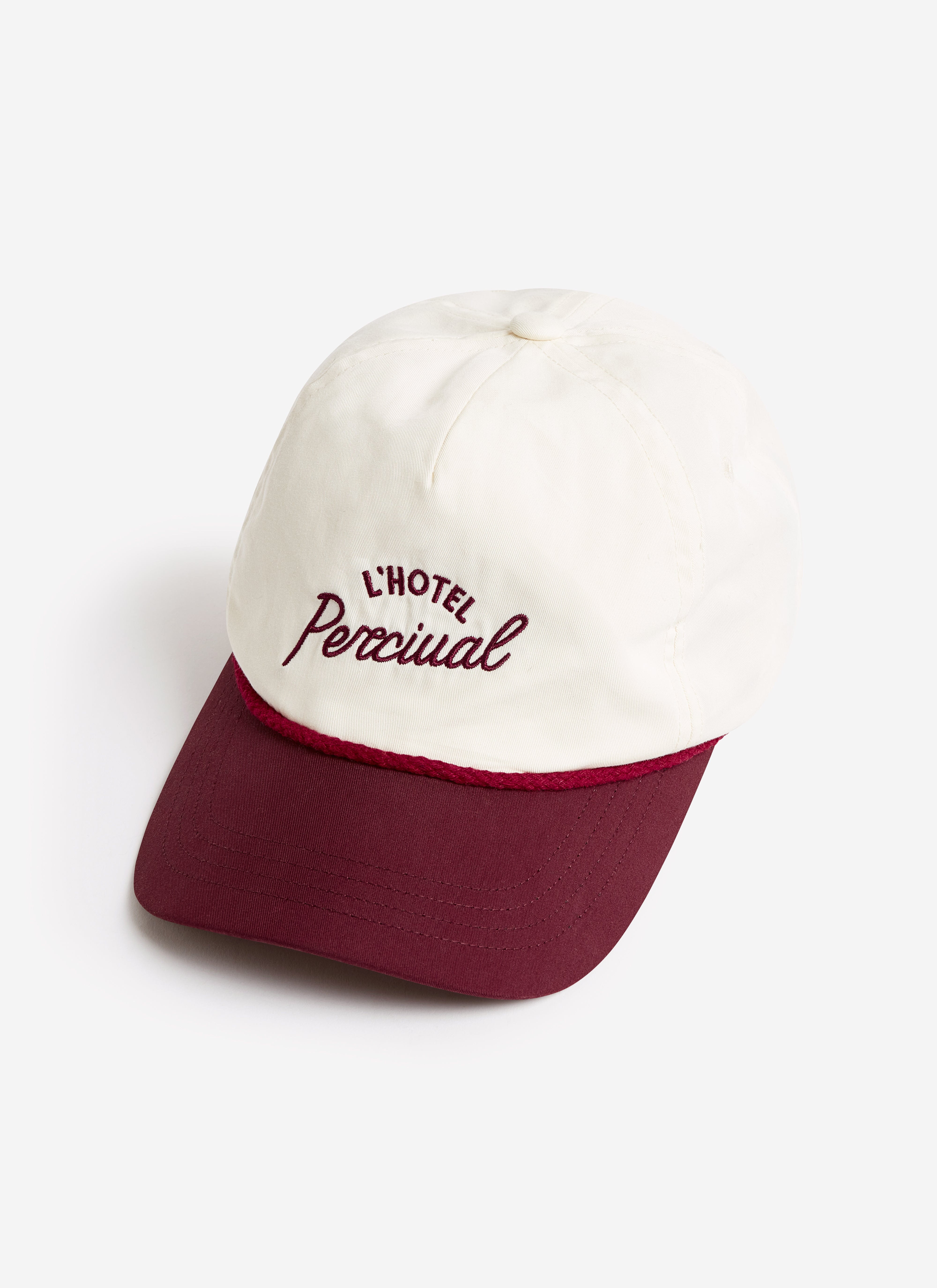 The L'Hotel Percival Soft Trucker Cap in ecru, featuring a contrasting burgundy peak and embroidered branding.