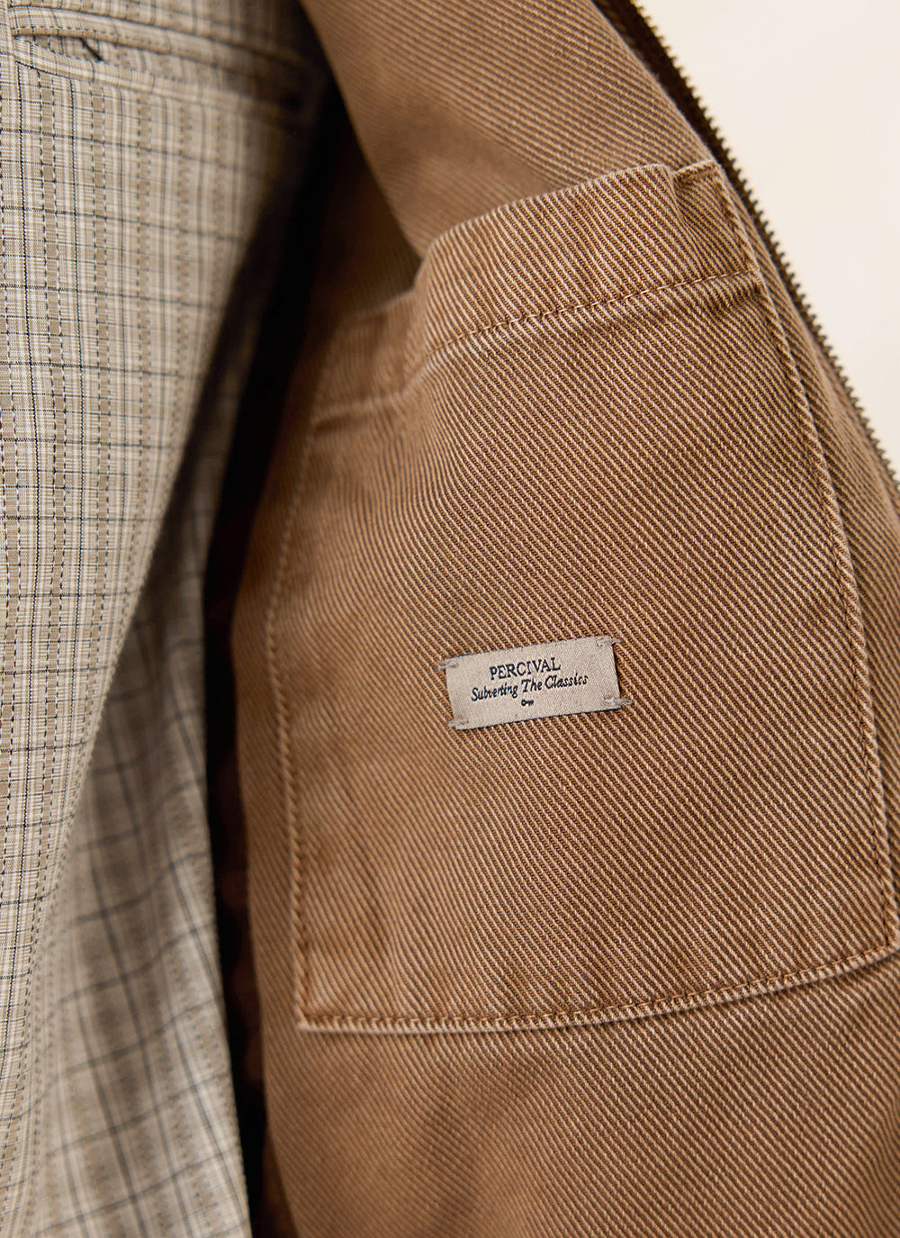 A close-up of the interior pocket and brand label on the mocha brown cotton twill jacket from Percival.