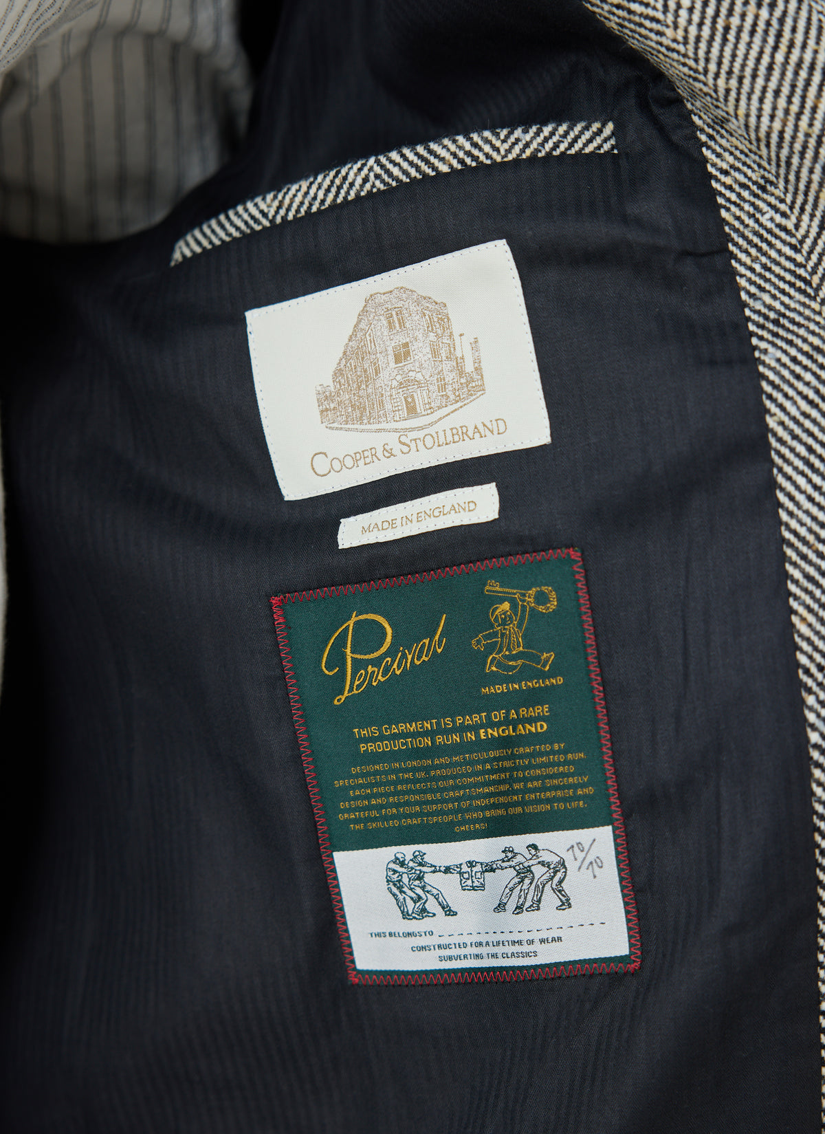 A close-up of the interior lining of the Percival grey wool car coat, showing Cooper & Stollbrand and Made in England labels.
