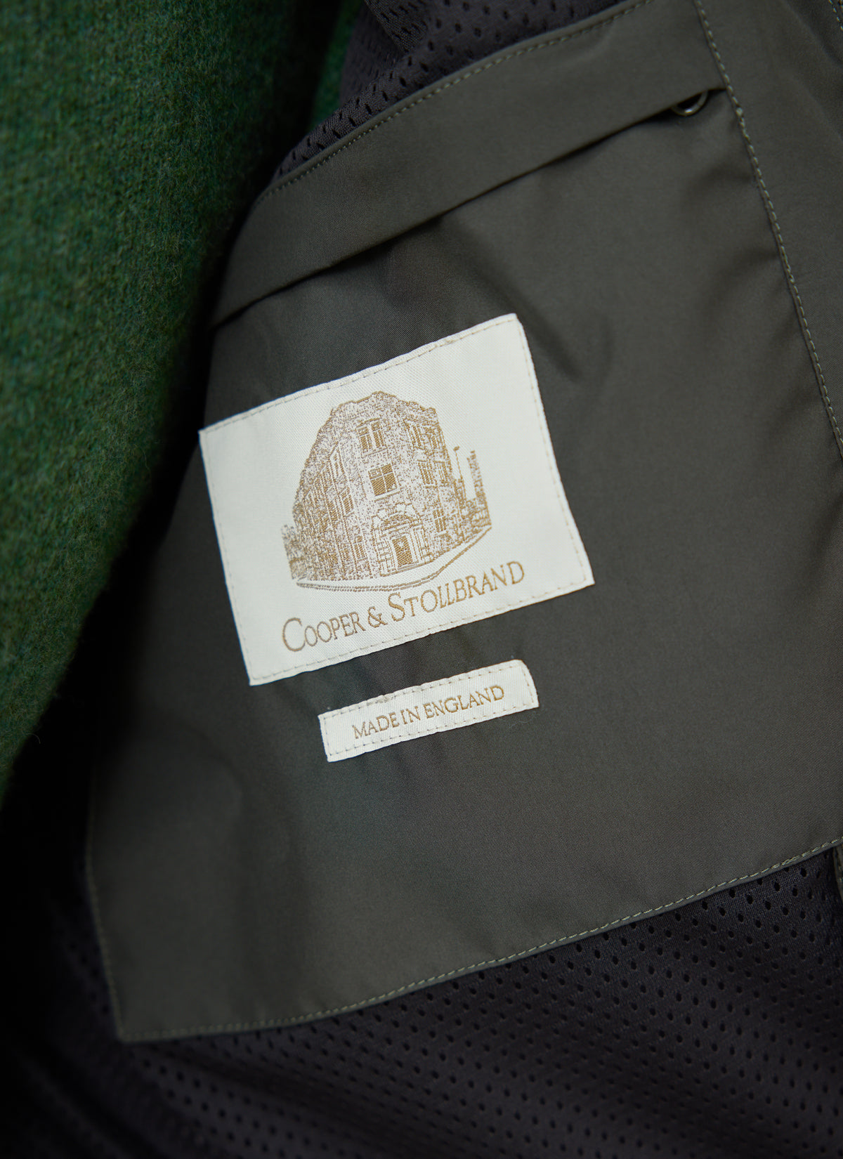 A close-up of the Cooper & Stollbrand label and Made in England tag inside Percival's forest green Hunter Jacket.