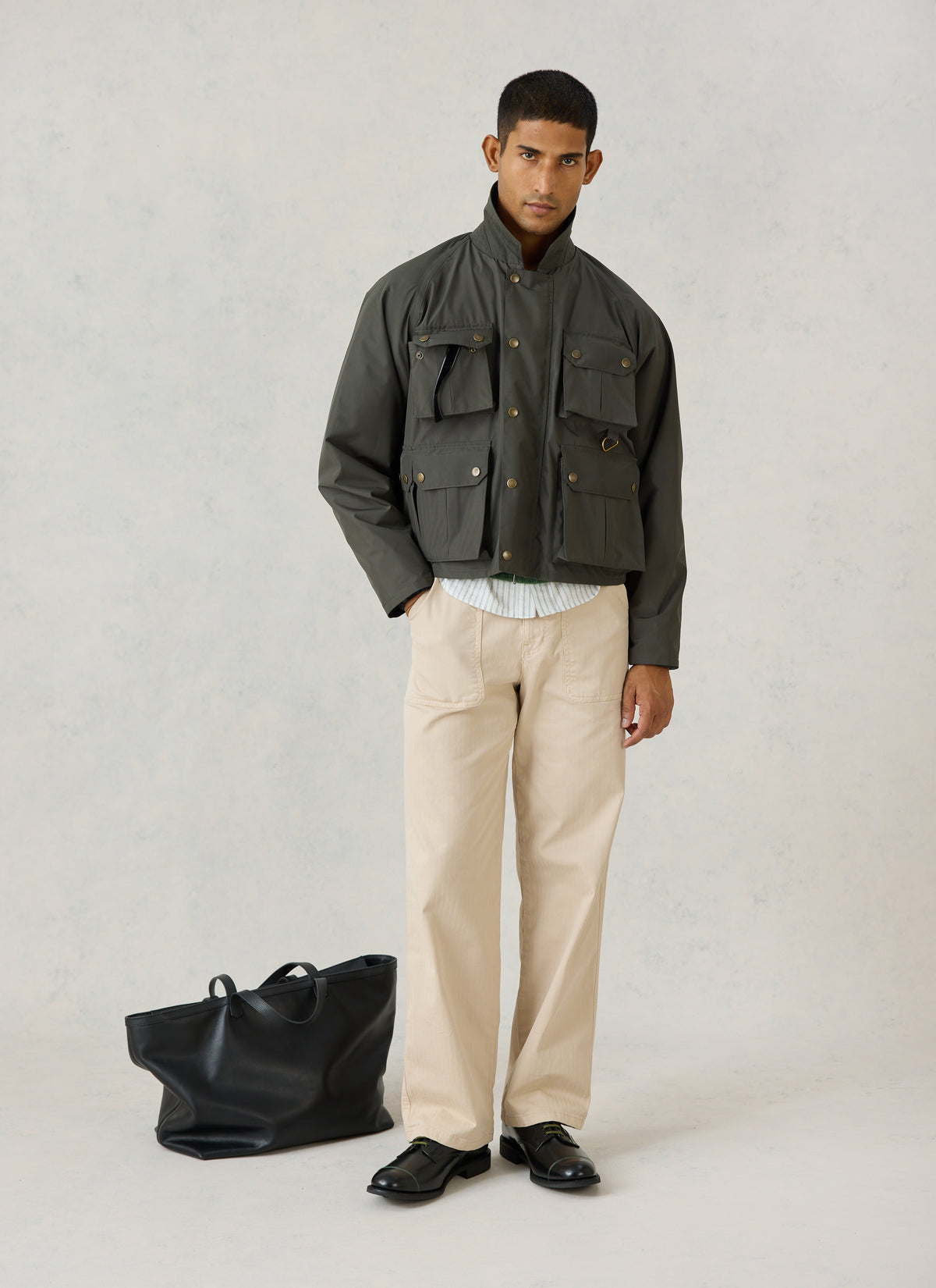 A model wearing Percival's forest green Hunter Field Jacket, paired with light trousers and a black tote bag.