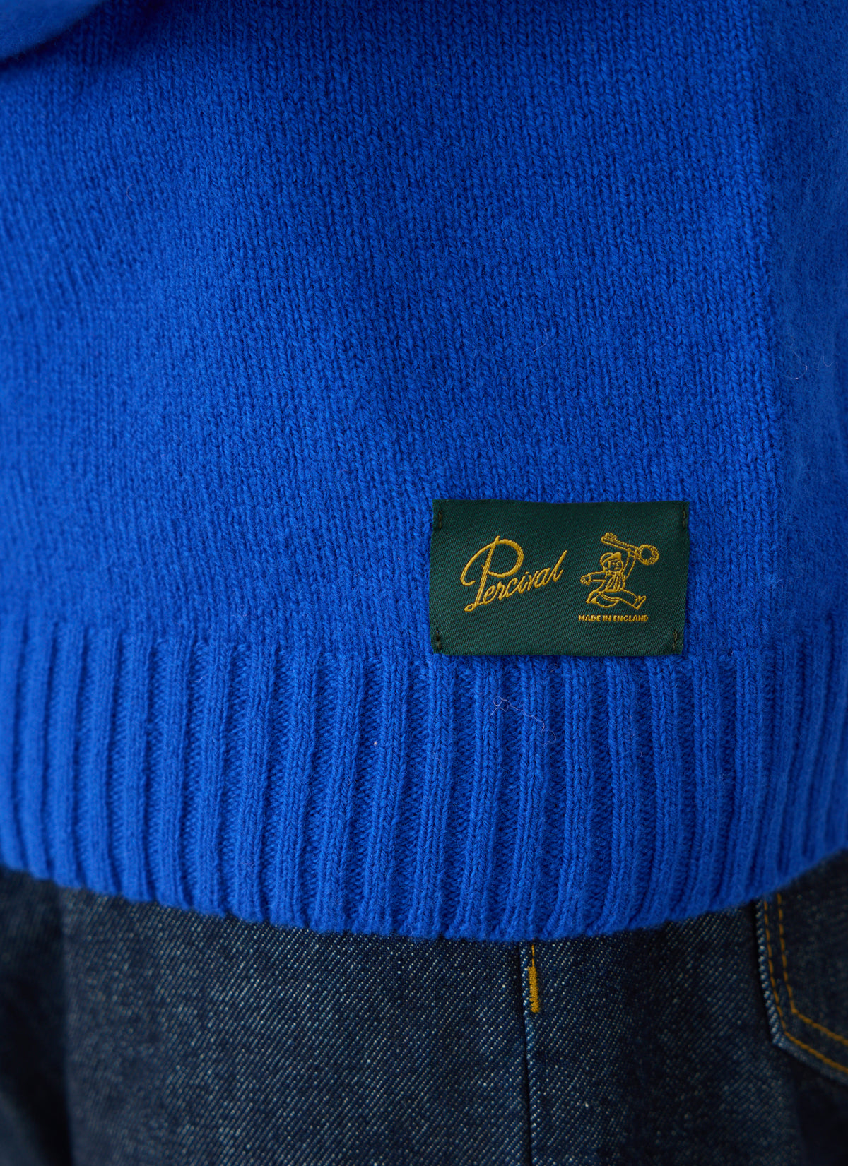 A close-up of the Percival cobalt blue lambswool jumper showing the ribbed hem and woven label.