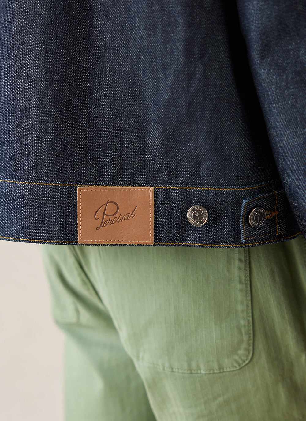 Close-up of the leather brand patch and metallic buttons on the raw denim Mackey Zip Jacket from Percival.