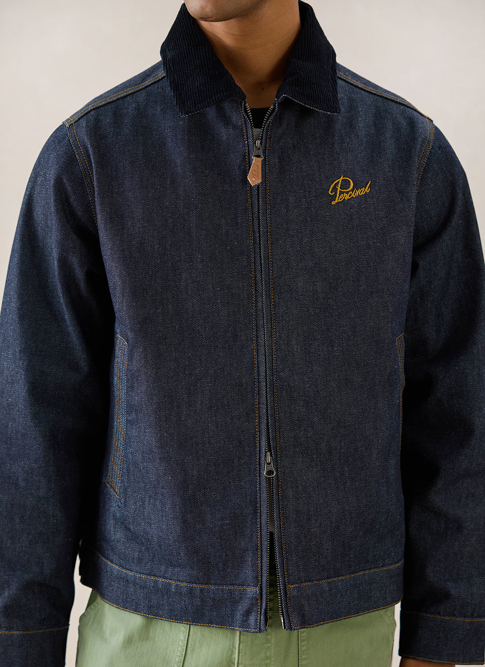 Close-up of a model wearing the raw denim Mackey zip jacket from Percival, showing the contrast collar and chest embroidery.