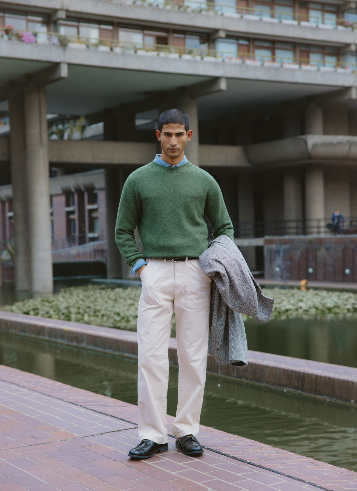 A model wearing the Percival forest green lambswool jumper, styled outdoors with light trousers and holding a coat.