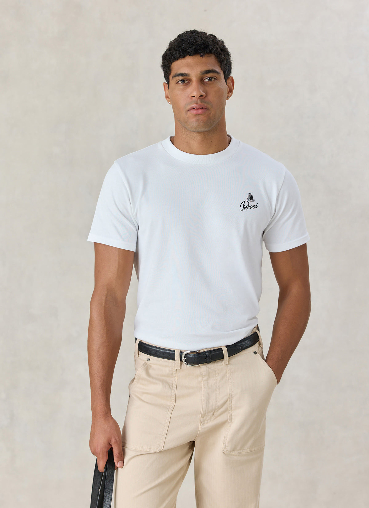 A model wearing the white Percival Martini Duo organic cotton t-shirt with a small chest print, paired with beige trousers.