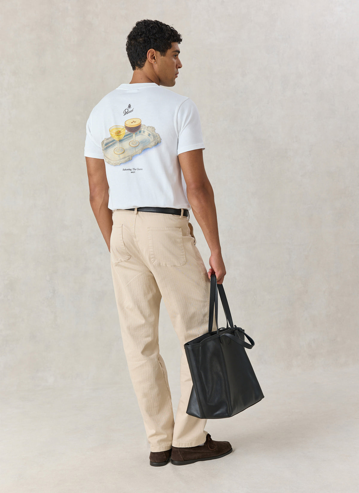 A model wearing the Percival white Martini Duo graphic T-shirt from behind, showing the cocktail back print and tote bag.