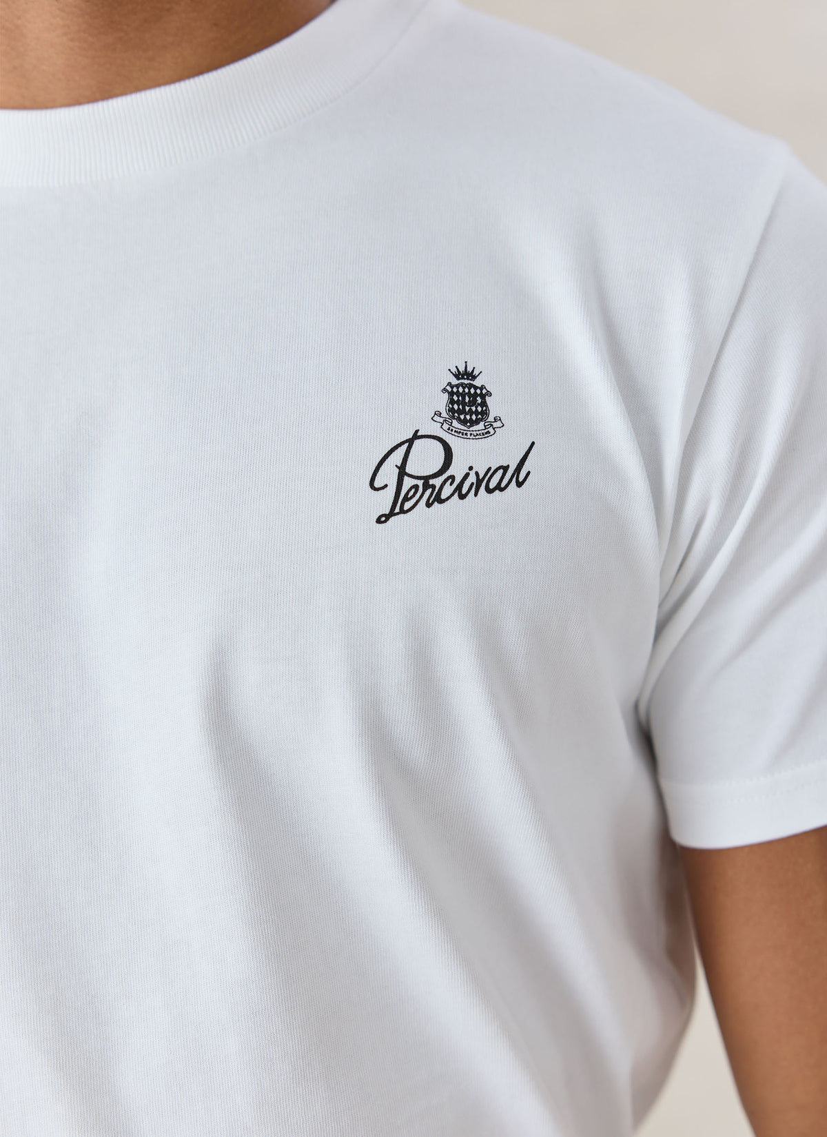 A close-up of the white Percival Martini Duo T-shirt showing the small black crest and script logo printed on the chest.