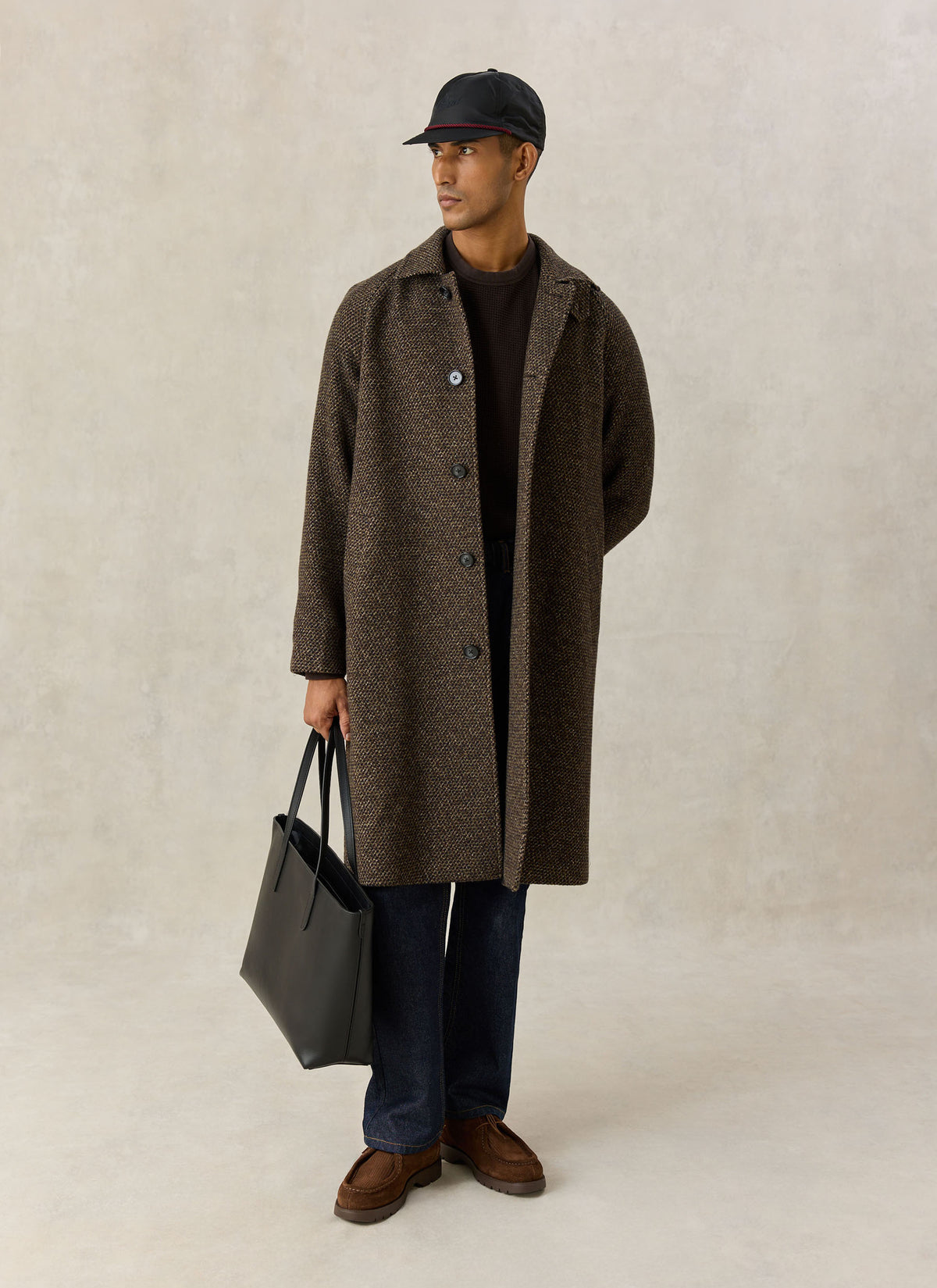 A model wearing the Percival brown fleck wool Mason car coat, holding a black leather tote bag against a neutral background.