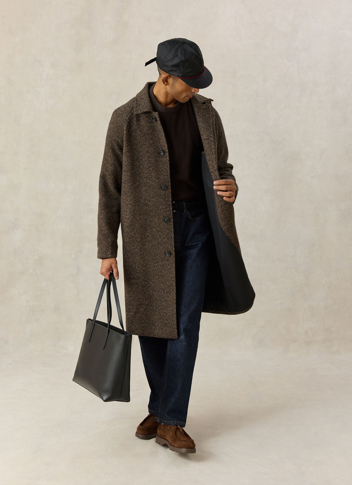 A model wearing the Percival brown fleck wool-blend car coat with dark trousers, a cap, and holding a black tote bag.