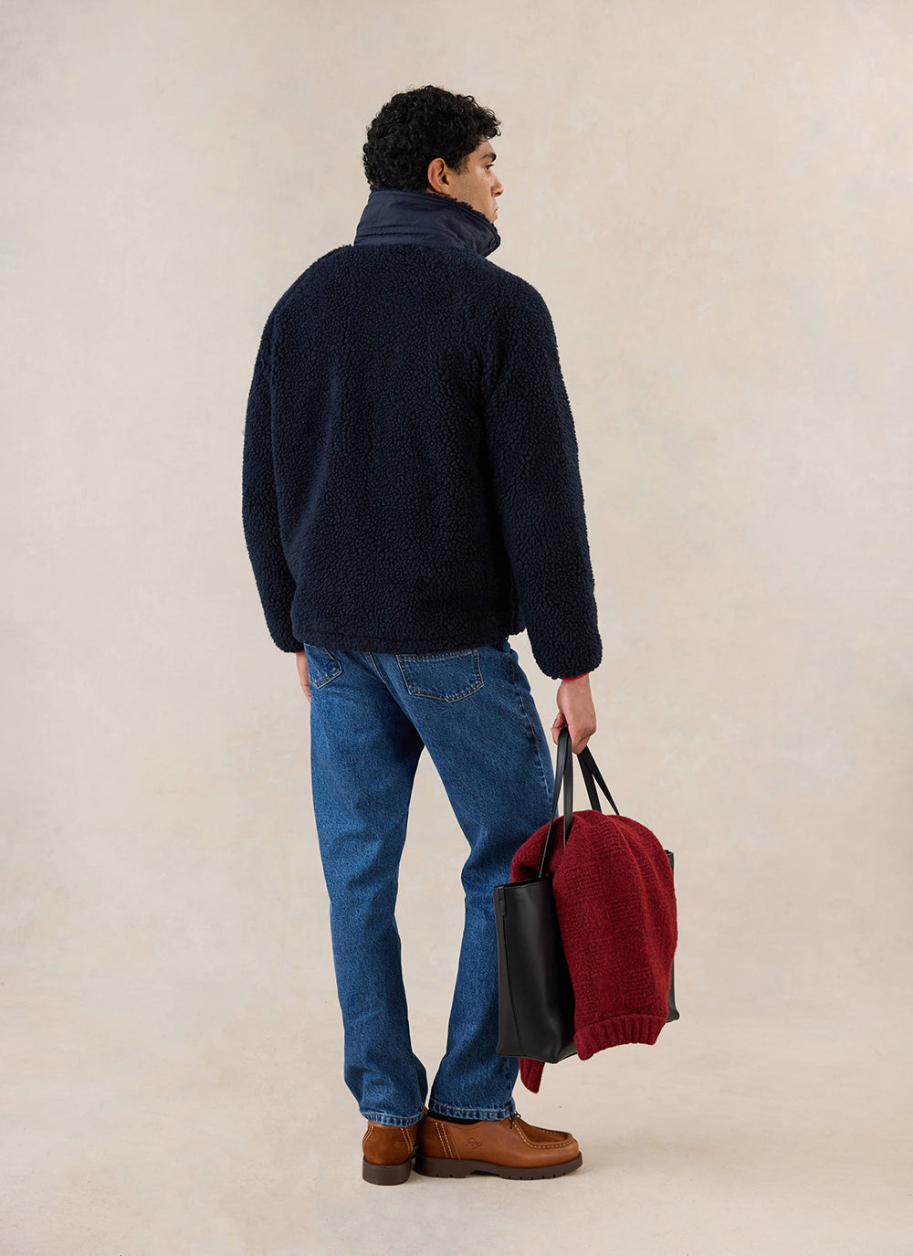 A model from behind wears the navy Percival fleece jacket, styled with blue jeans and holding a black tote bag.