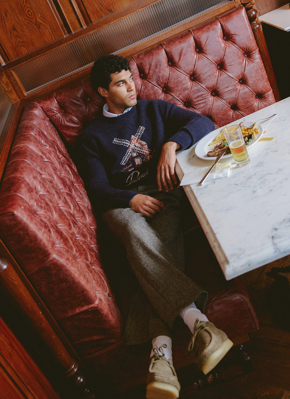 A model wearing the navy Percival Miller Jacquard jumper and trousers while sitting in a leather booth at a restaurant.
