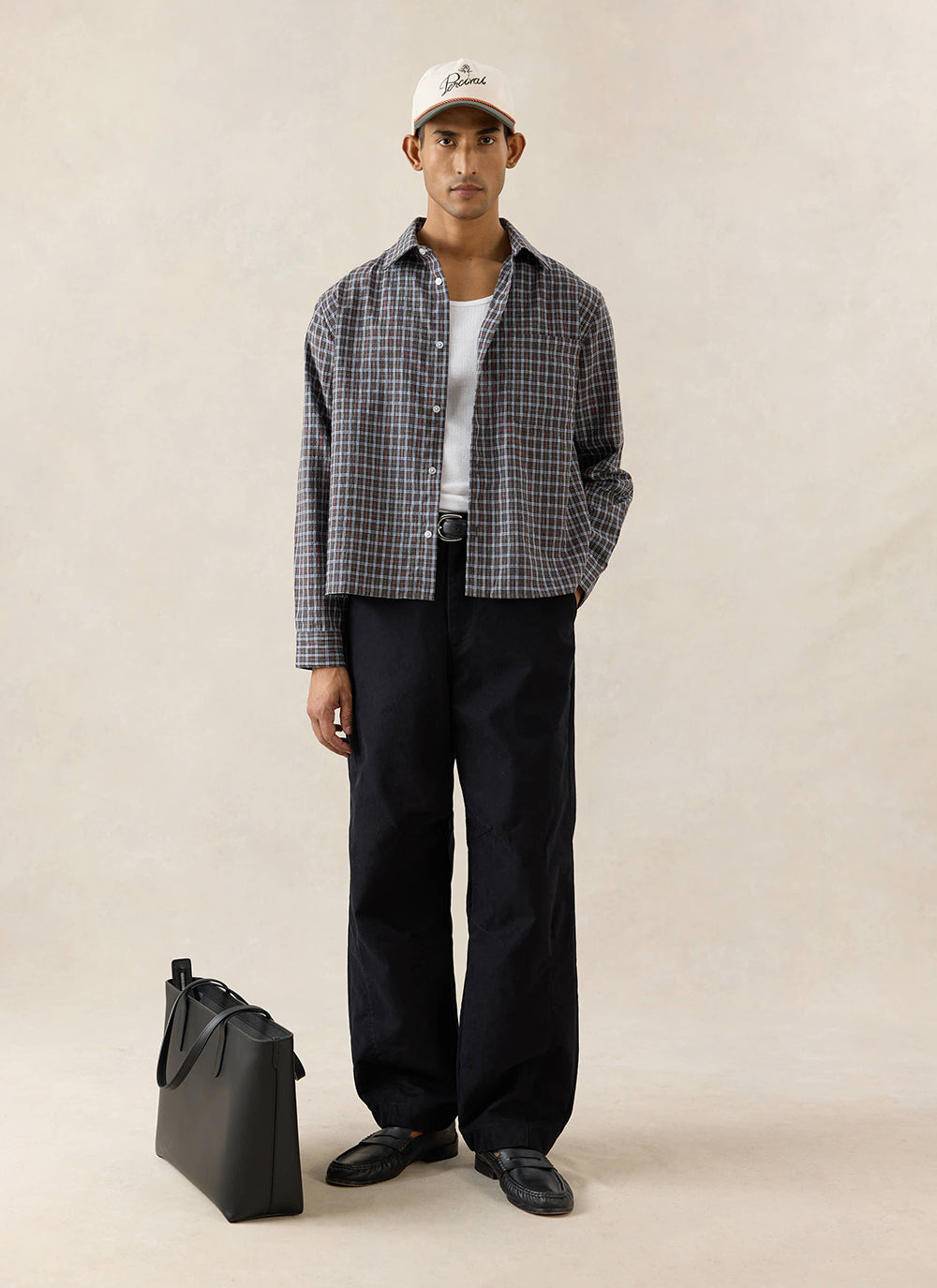 A model wears the black Percival Milo Relaxed Barrel Leg Trousers, styled with a checked shirt, vest and loafers.