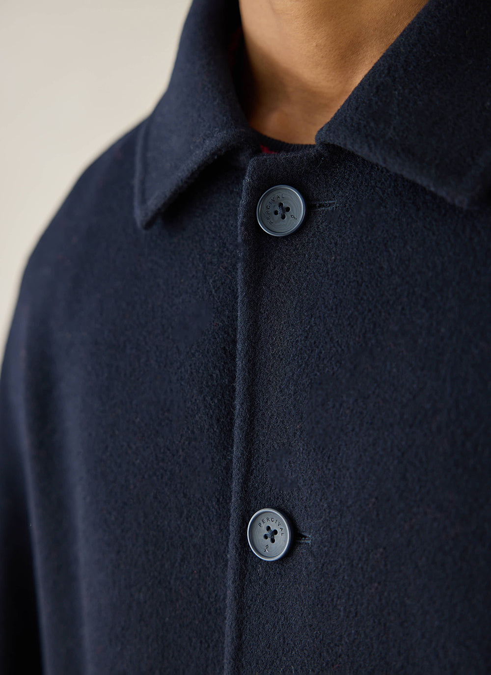 Close-up of the collar and branded buttons on the navy wool Percival Minnesota Overcoat worn by a model.