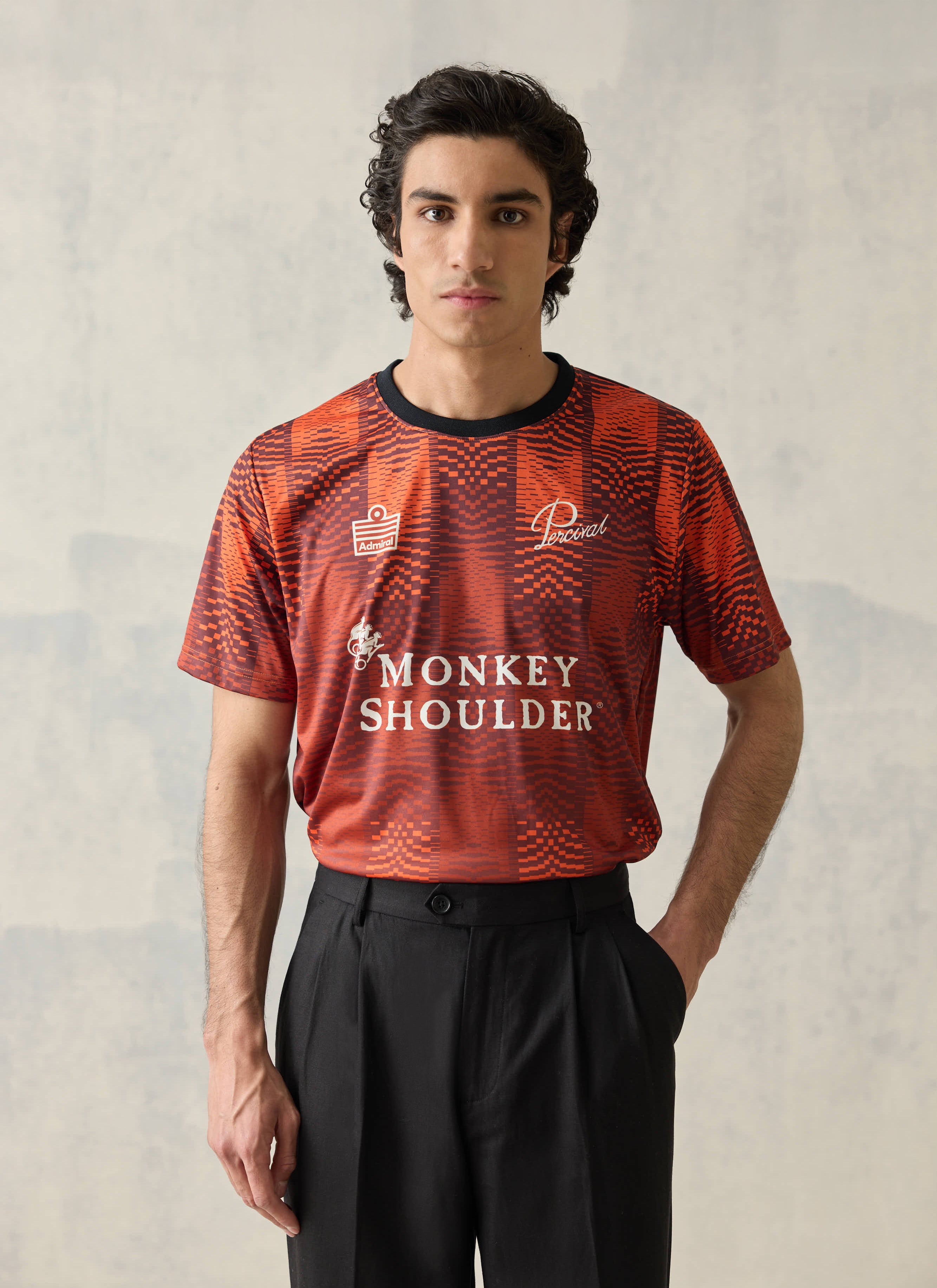 Orange Percival x Monkey Shoulder football shirt featuring pixel-distortion stripes and branding, worn by a male model.