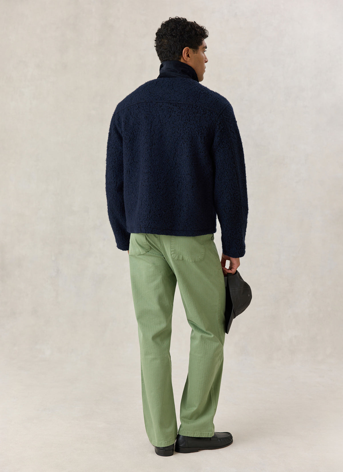 A model from the back wearing the Percival navy wool-blend Murrey fleece jacket with a cord collar and green trousers.