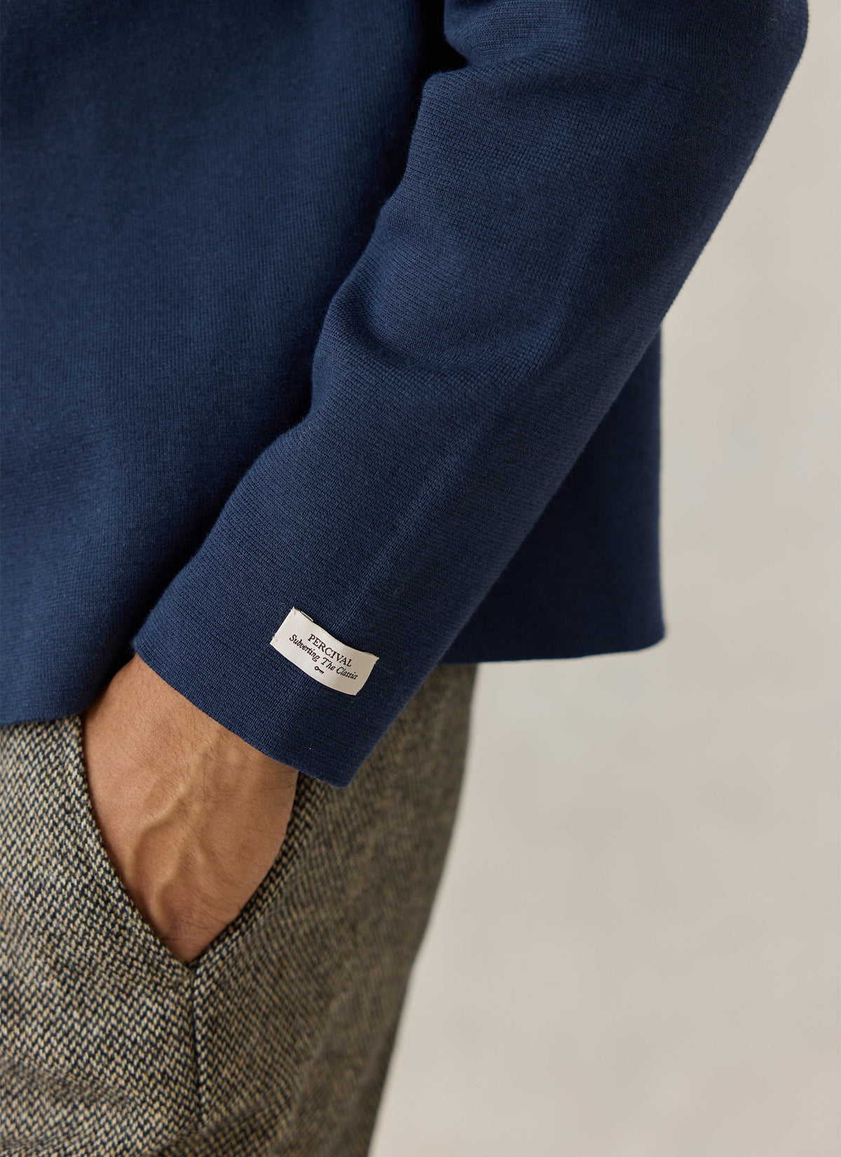 A close-up of the Percival navy Nixon knit cardigan sleeve, showing the woven label and textured cotton-blend fabric.