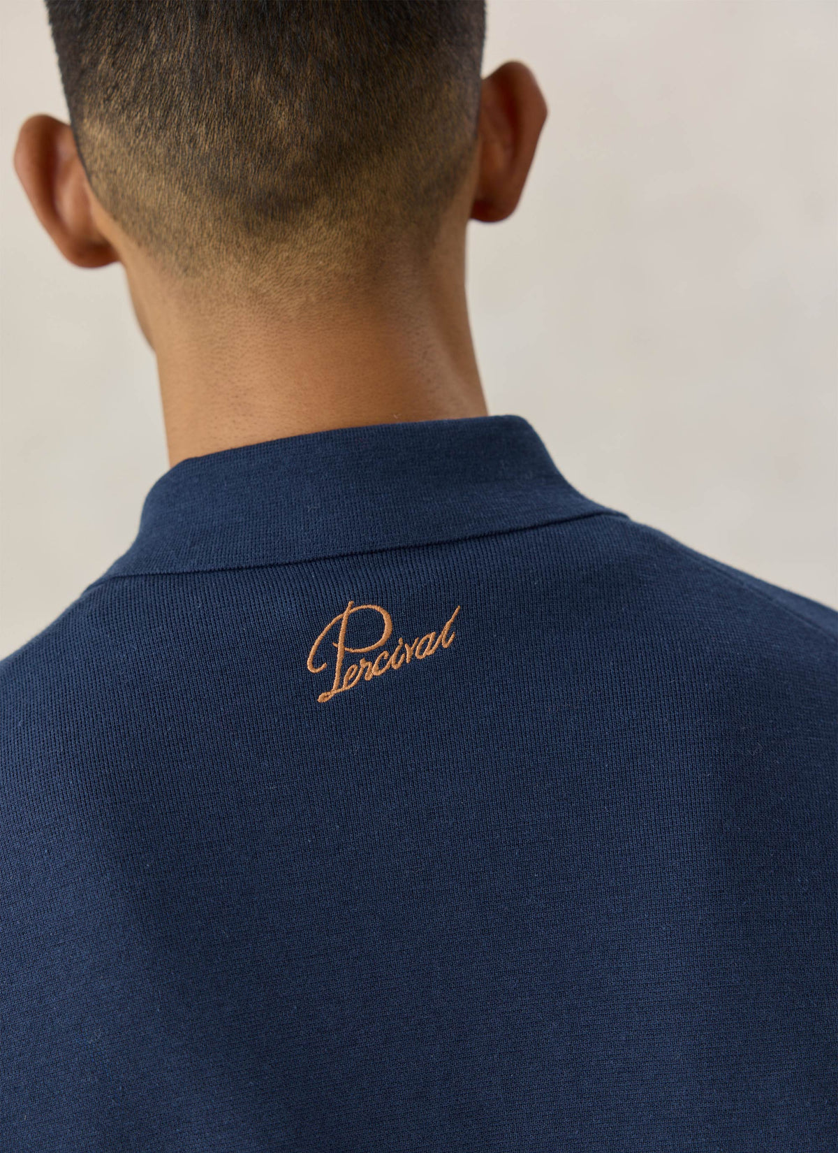 Close-up of the back neck on the Percival navy blue Nixon knit collared cardigan, showing the embroidered logo detail.