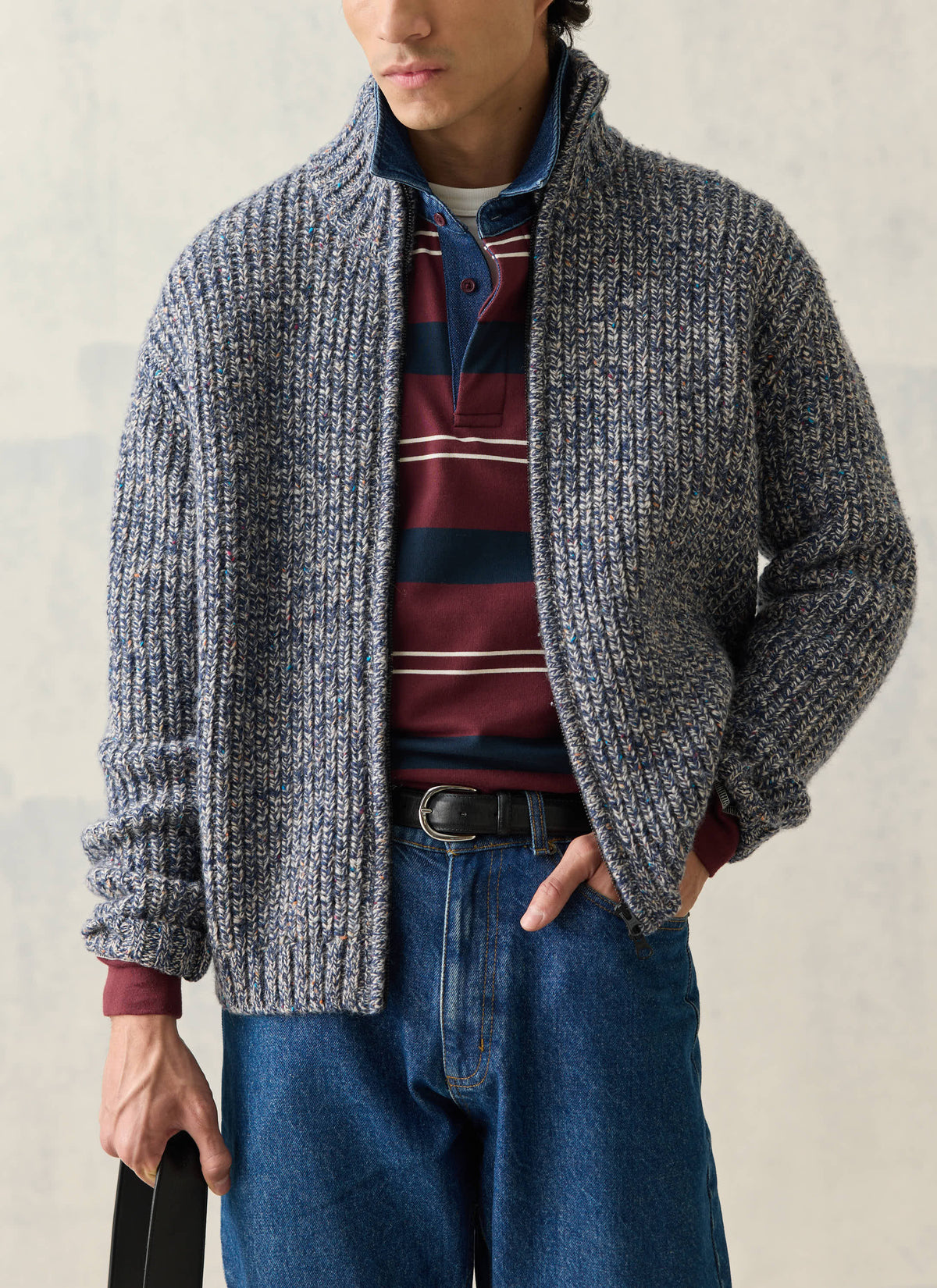 A model wearing the Percival blue fleck Norton ribbed fisherman zip cardigan over a striped polo and blue jeans.