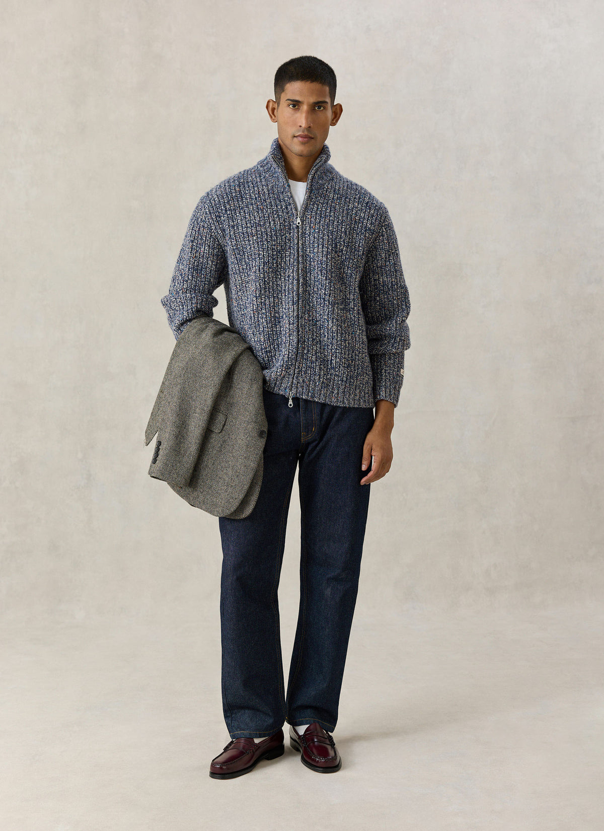 A model wearing the Percival blue fleck Norton ribbed zip cardigan with dark jeans, holding a tweed jacket.