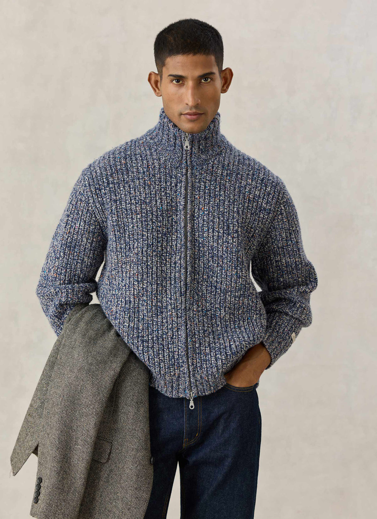 A model wearing the Percival blue fleck Norton ribbed zip cardigan in alpaca wool while holding a tweed jacket.